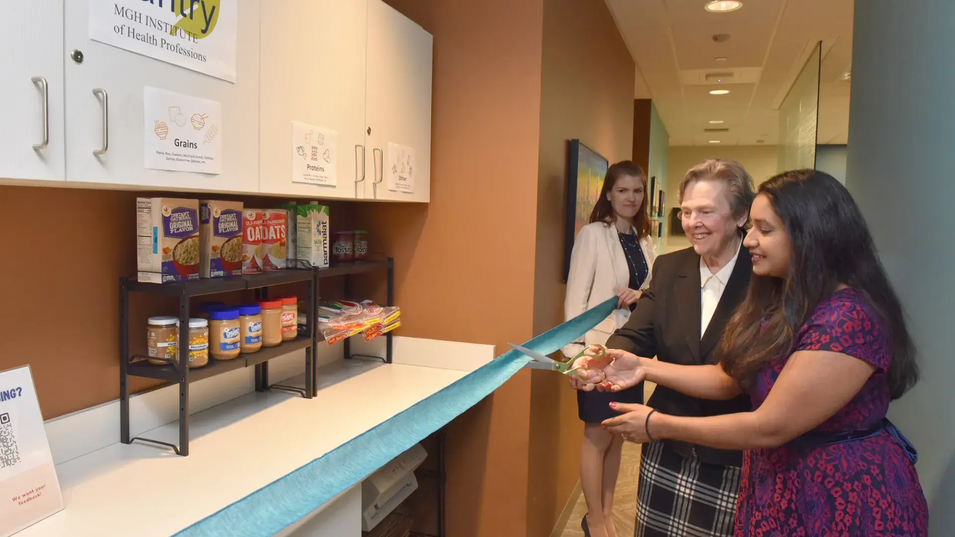 one woman holds a long ribbon while two others cut it