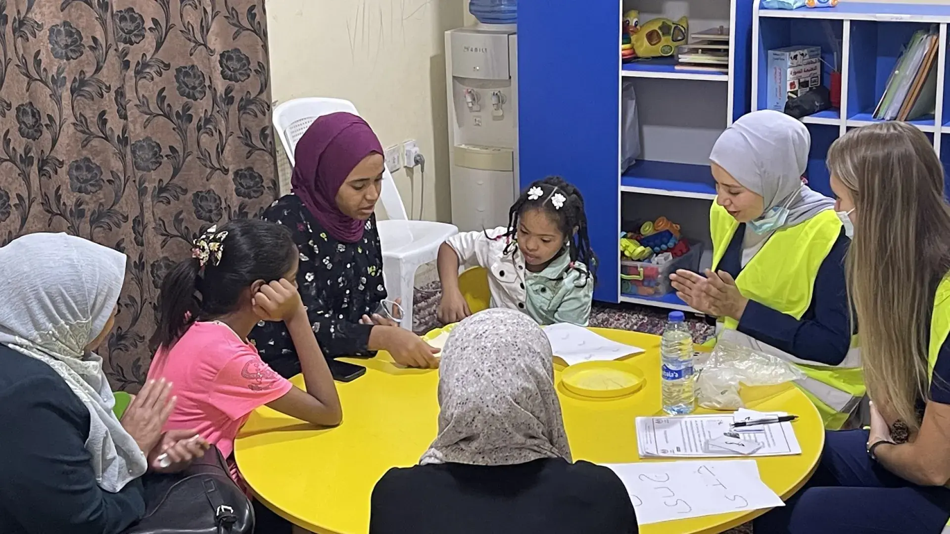 group of women wearing hajibs sit at a table with children