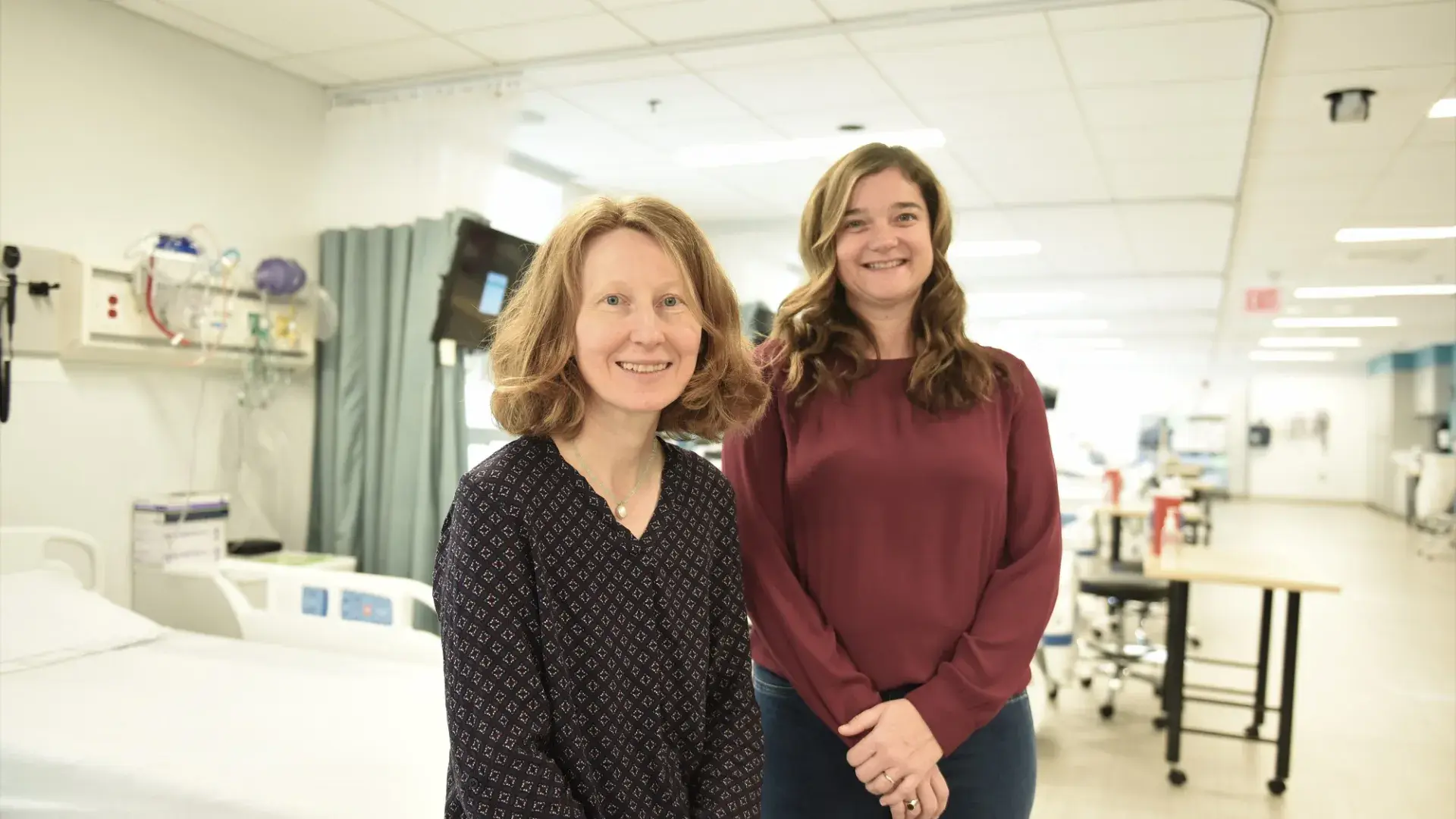 woman sits on stretcher in hospital hallway while another woman stands behind