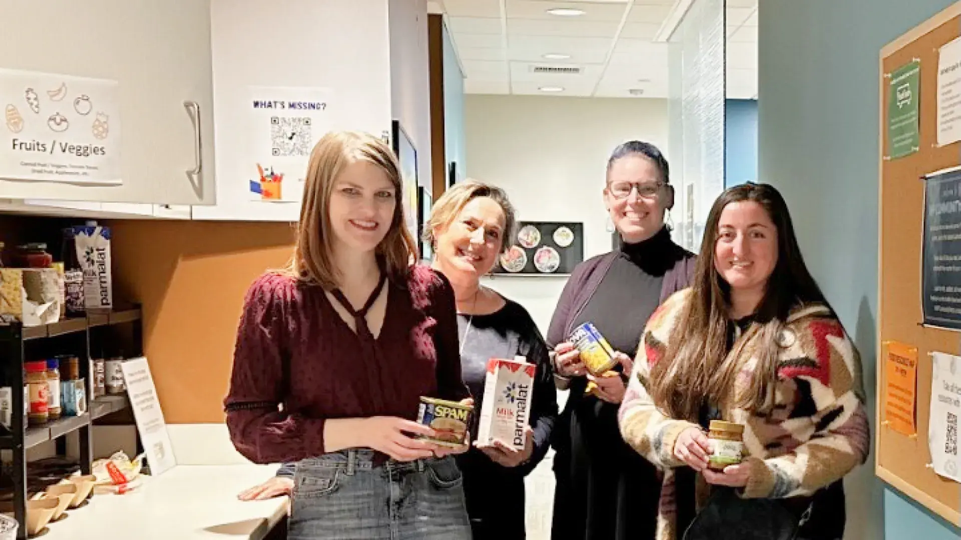 women pose with cans of food in their hands next to a cabinet