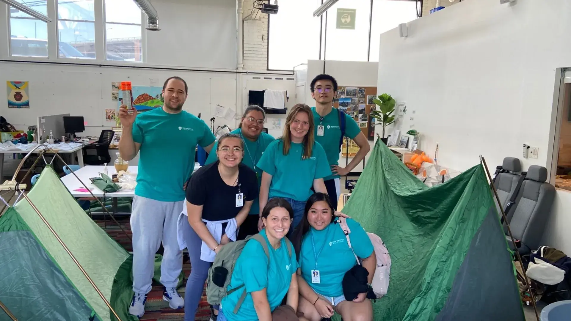 students pose in a high ceilinged gym with tents made of green tarps
