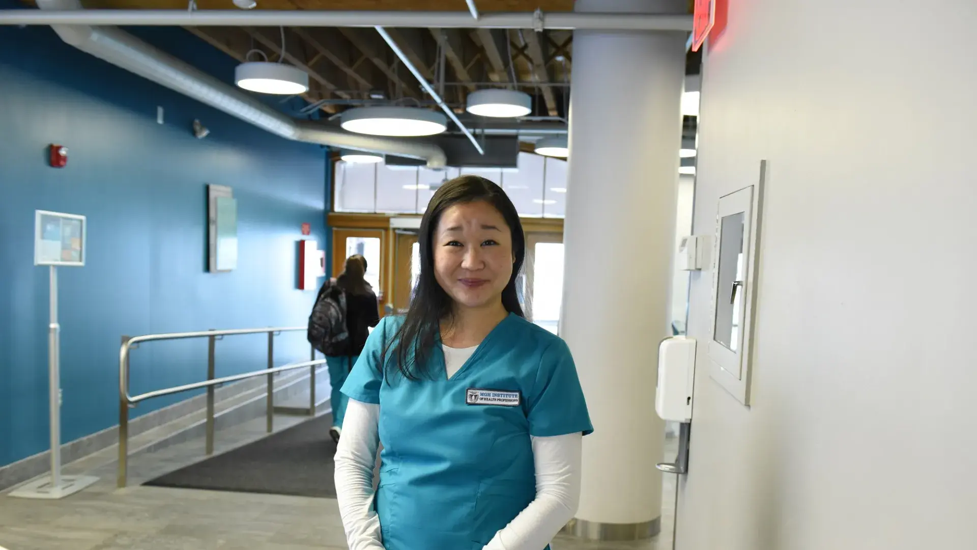 kanayo stands in a hallway wearing blue scrubs