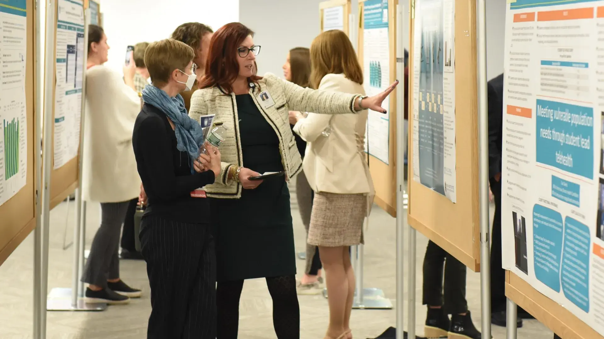 woman points to giant bulletin board with poster on it while another woman looks on