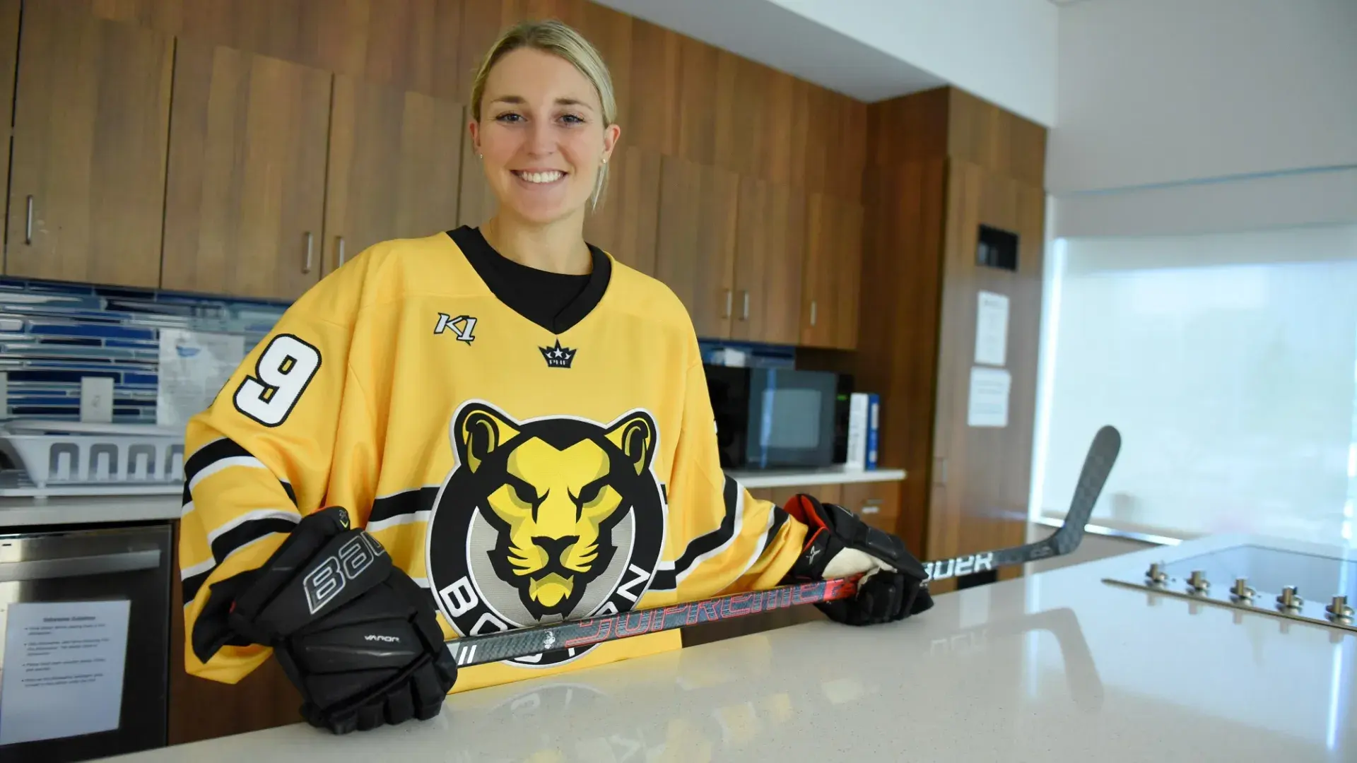 sammy stands at the occupational therapy kitchen counter in her yellow hockey jersey holding a hockey stick