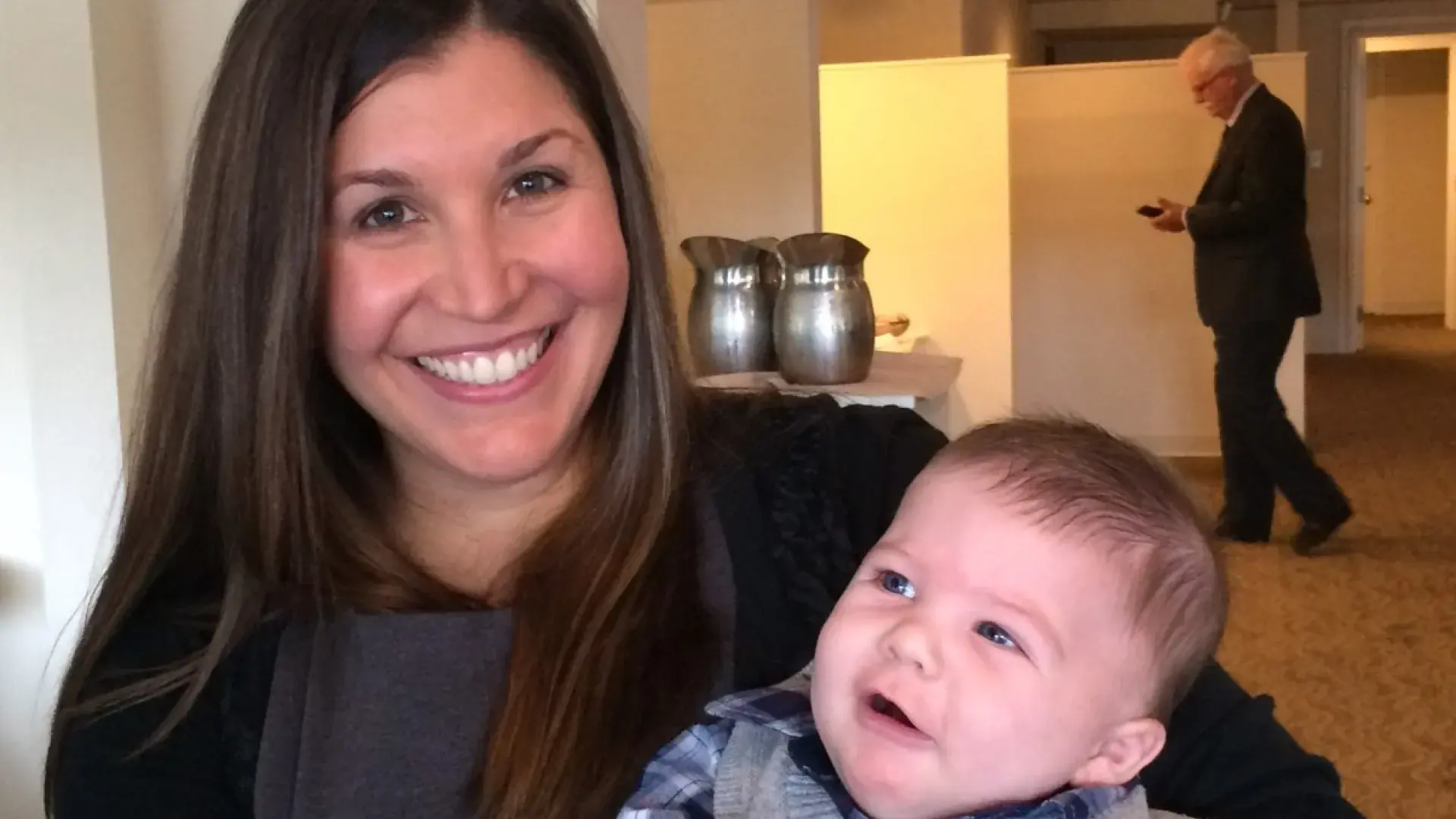 rebecca holds a baby in a sweater vest with a cute puzzled look on his face