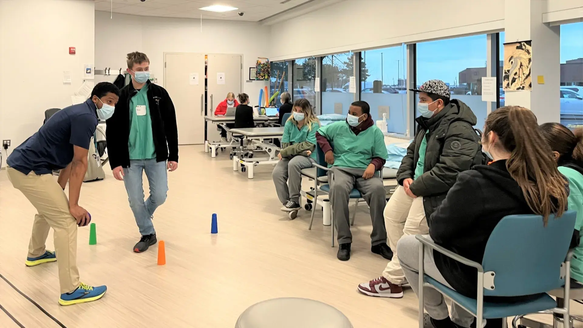 man squats with a ball in his hand while 5 people seated watch him