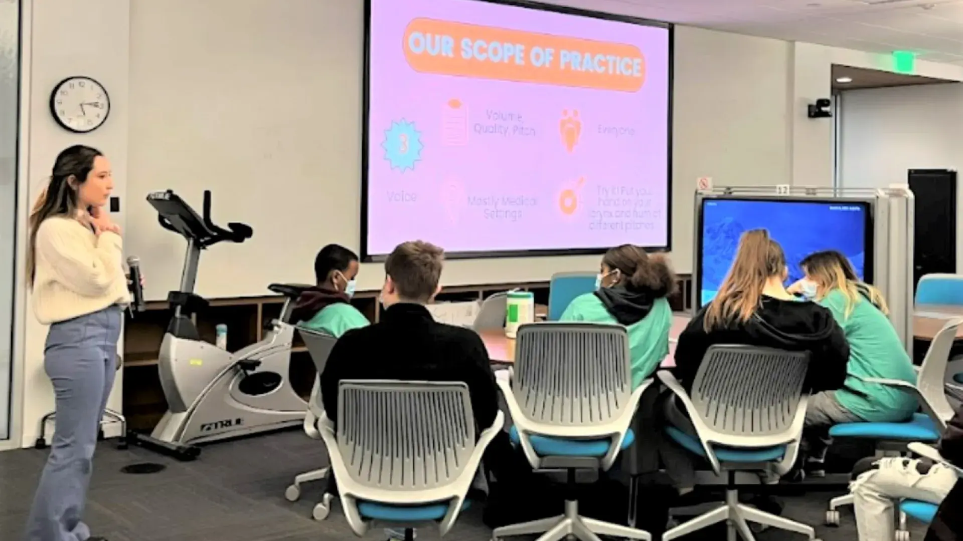 woman stands in front of an audience looking at a screen that says "our scope of practice"