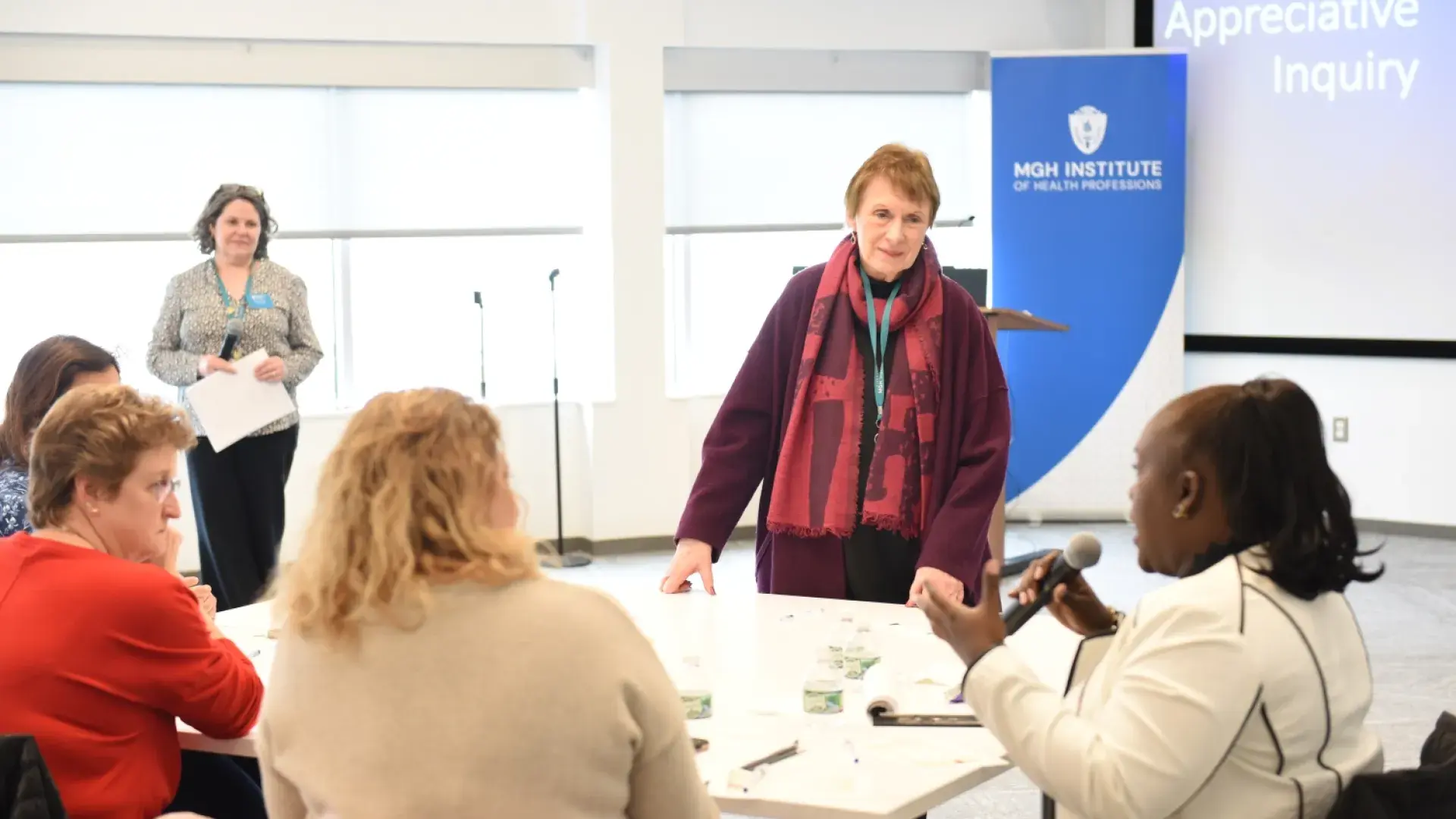 women in a bright room listen to a woman seated holding a microphone