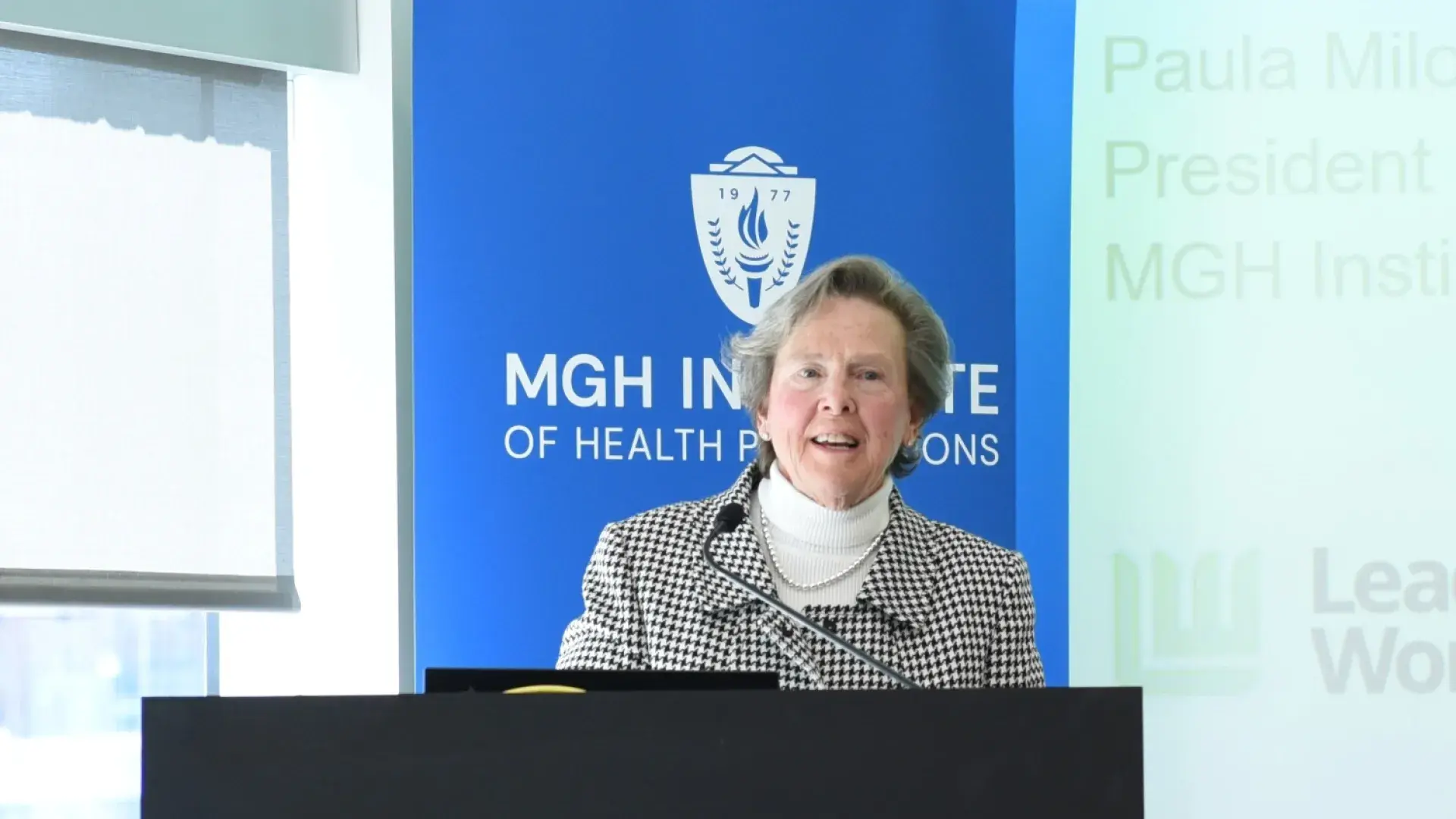 woman in a black and white checked blazer stands at a black podium