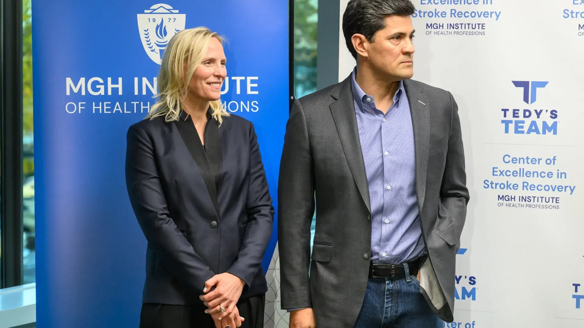 tedy and heidi stand in front of a MGH IHP banner with thoughtful looks