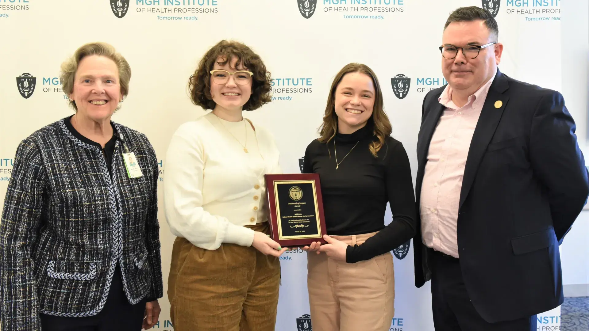 danielle has a cream top and olivia has a black turtleneck and they both hold the award plaque