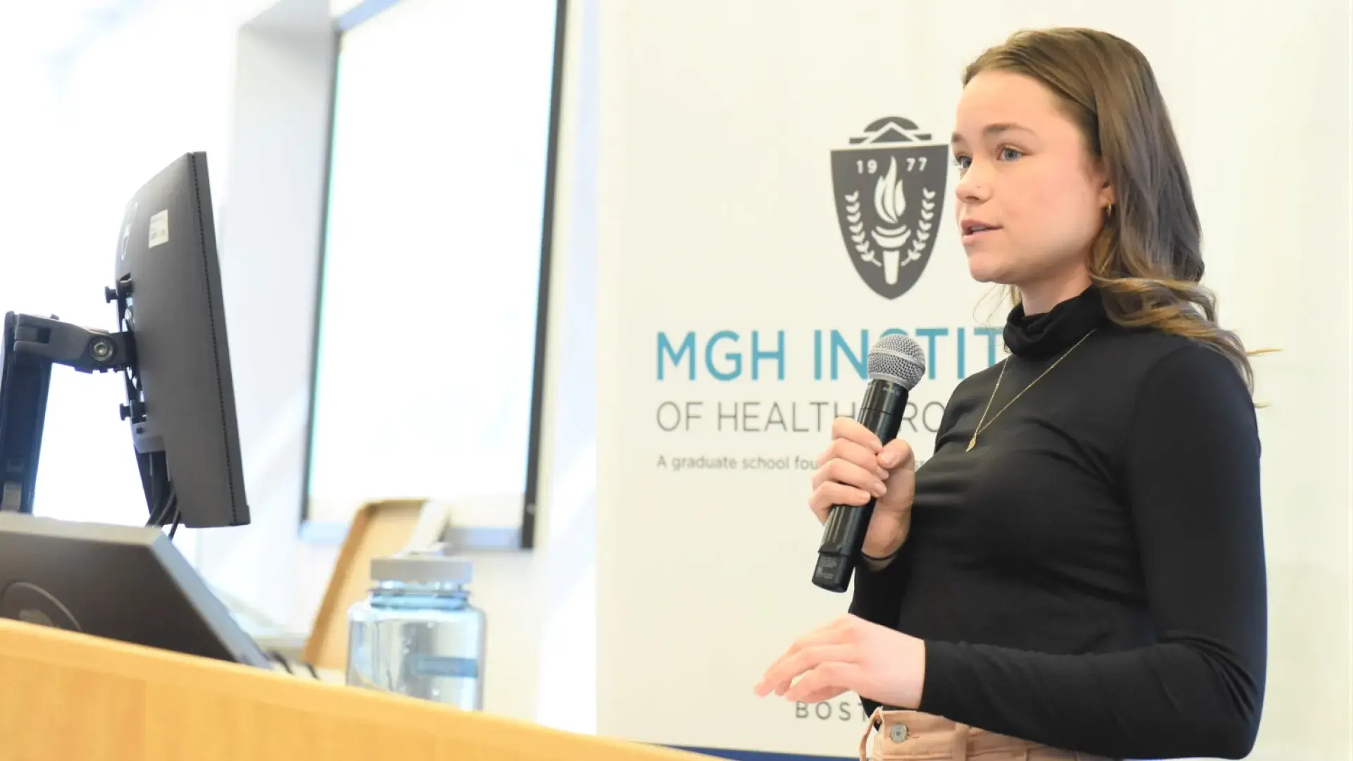 olivia wears a black turtleneck shirt and stands at the podium