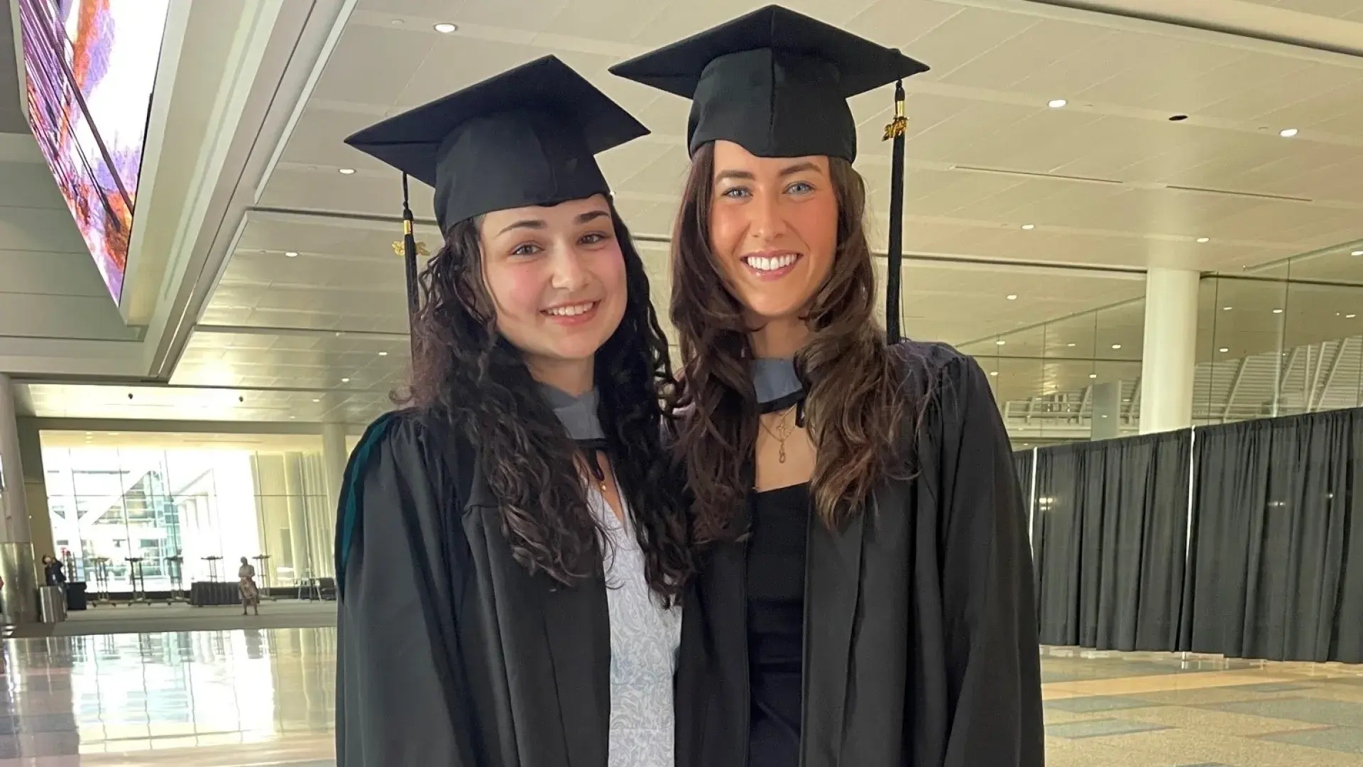 the women stand together smiling in a hallway wearing black graduation caps and gowns