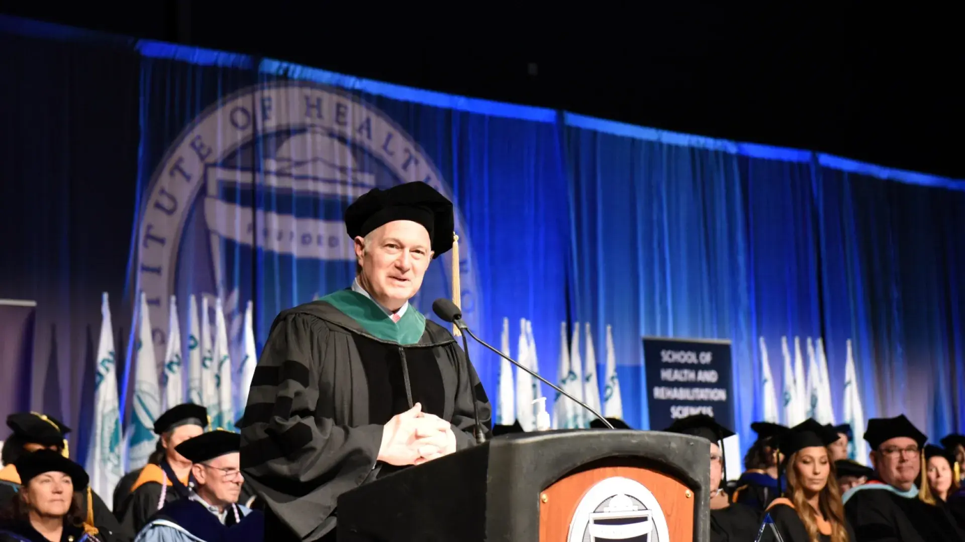 man at podium in green and black regalia 