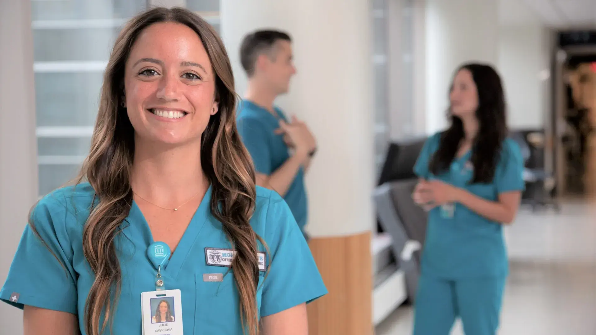 Julie wears blue MGH scrubs and stands in a hospital hallway