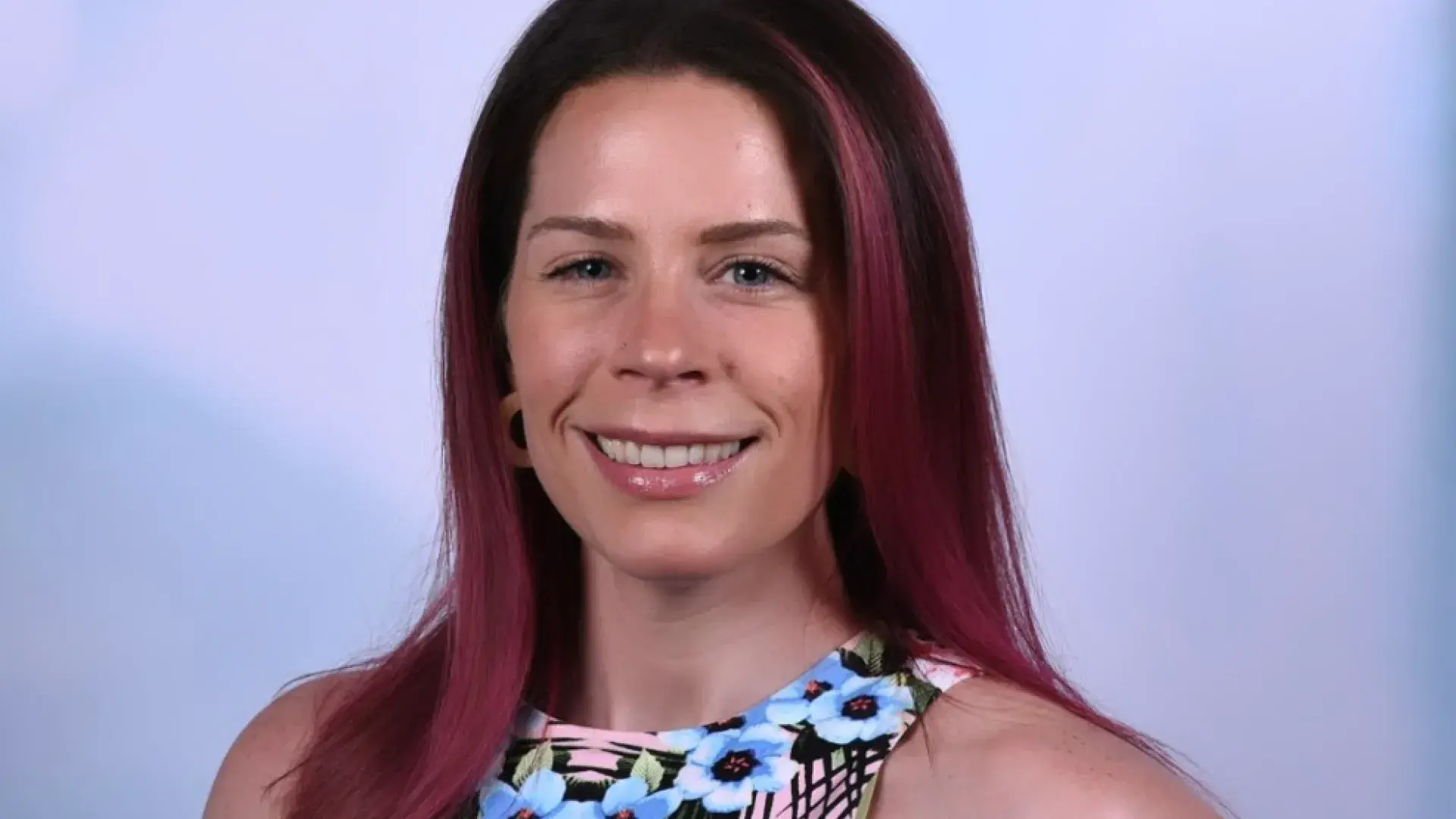 Brenna Morse has dark red hair and stands in front of a purple background