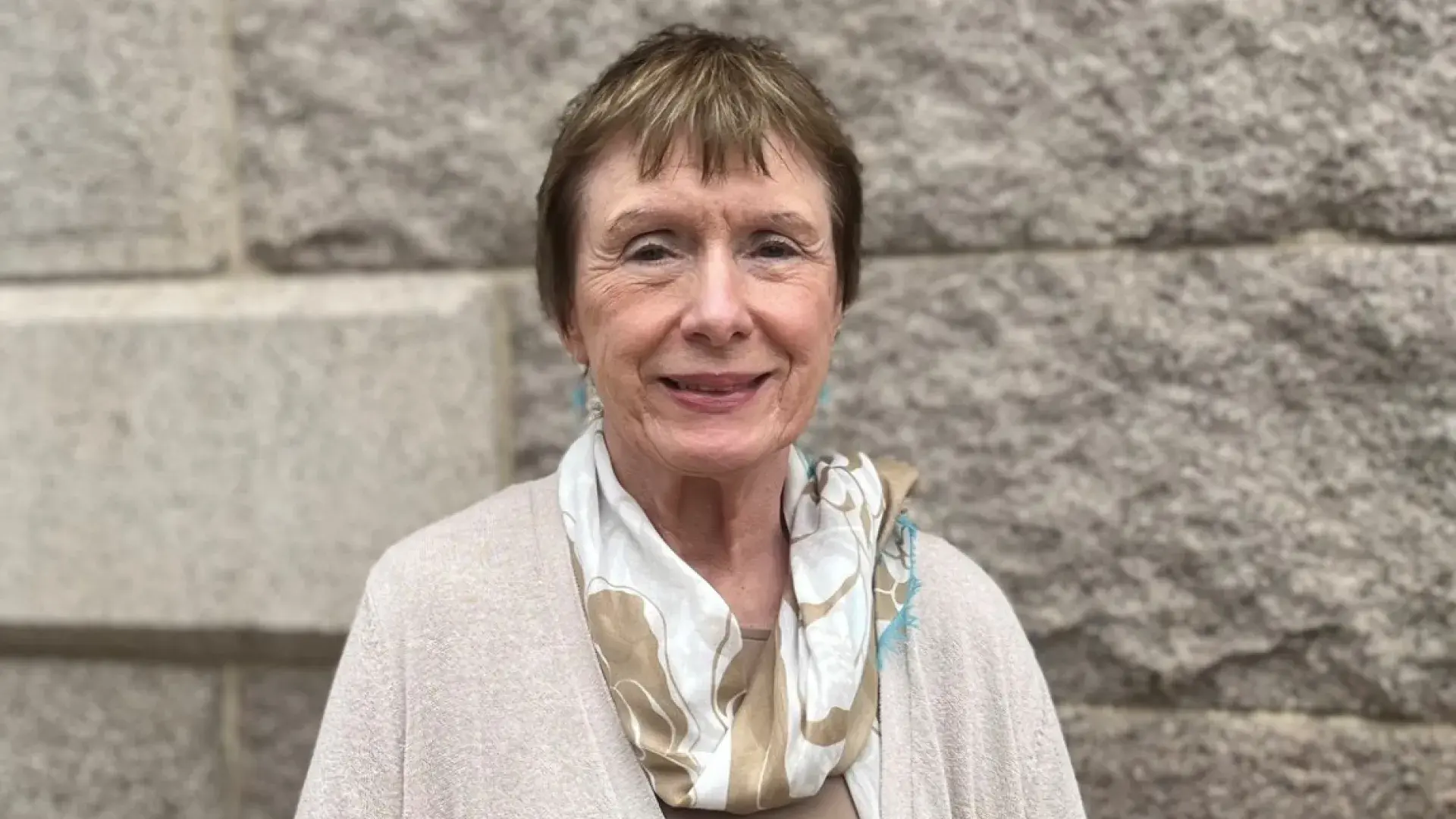 margie wears a beige sweater set and patterned silk scarf