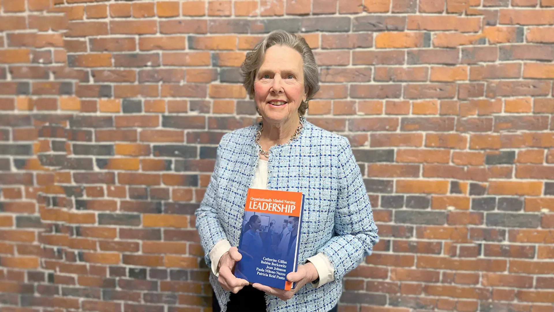 paula stands in front of a brick wall with her book