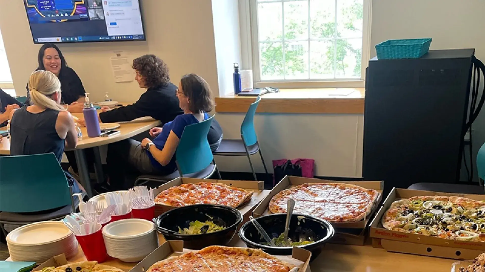 open boxes of pizza on a table in front of a table where a team sits with family feud on the TV