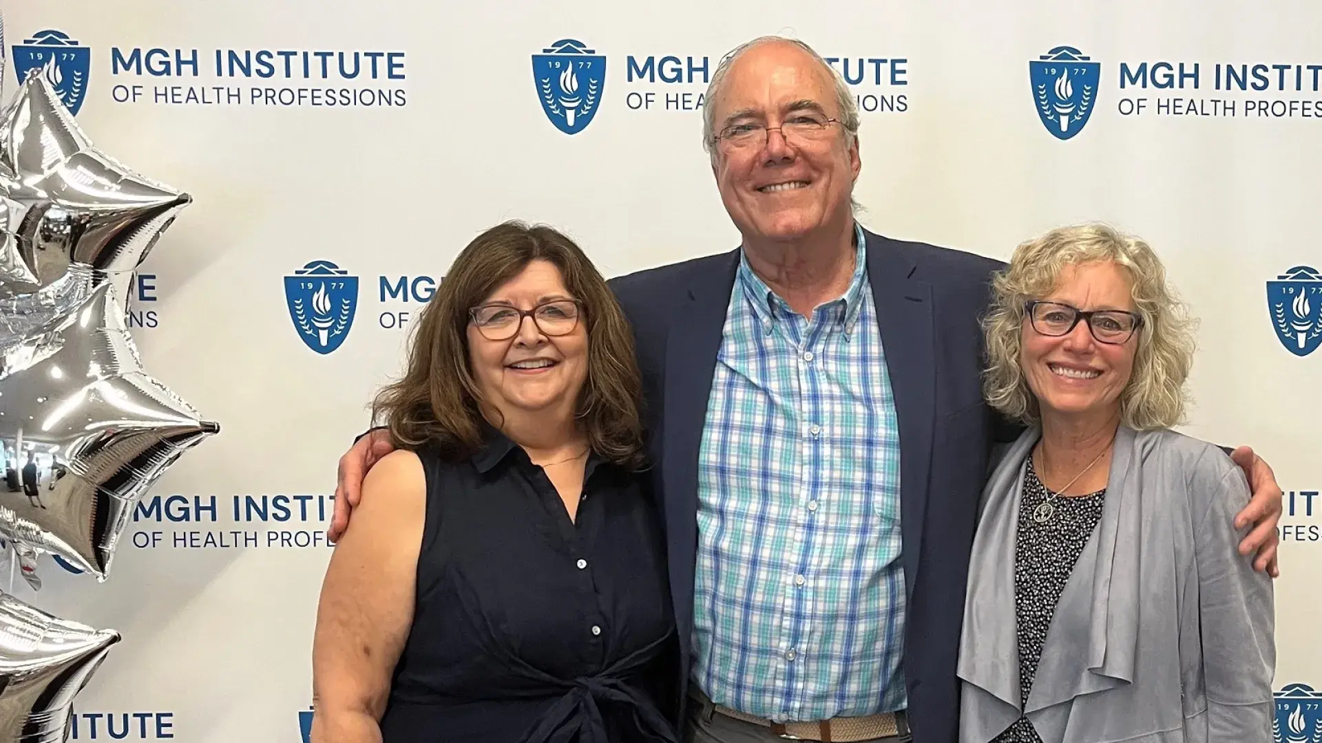 charley stands with his arms around the two ladies next to some silver balloons