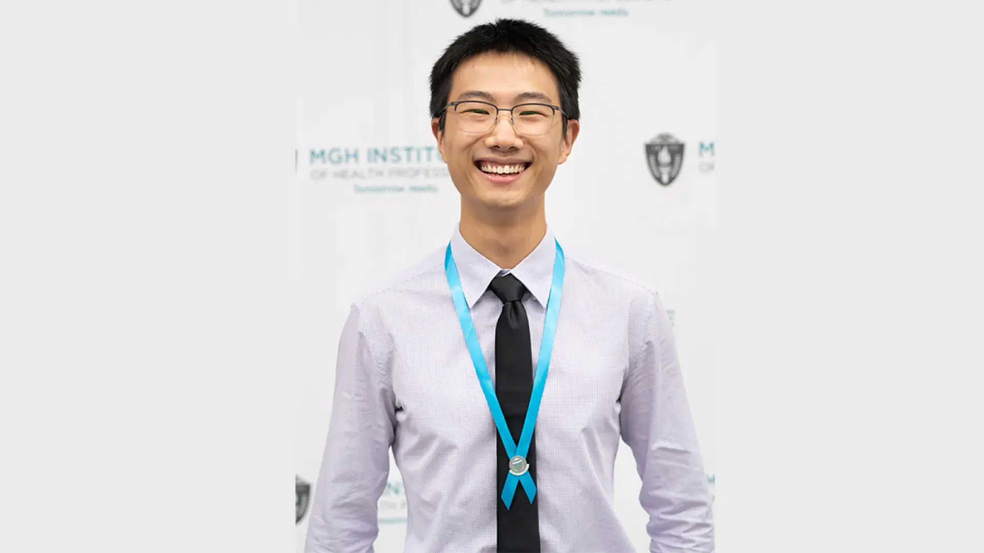 Asian man with black hair and glasses wears a black tie and off white collared shirt with a teal ribbon around his neck