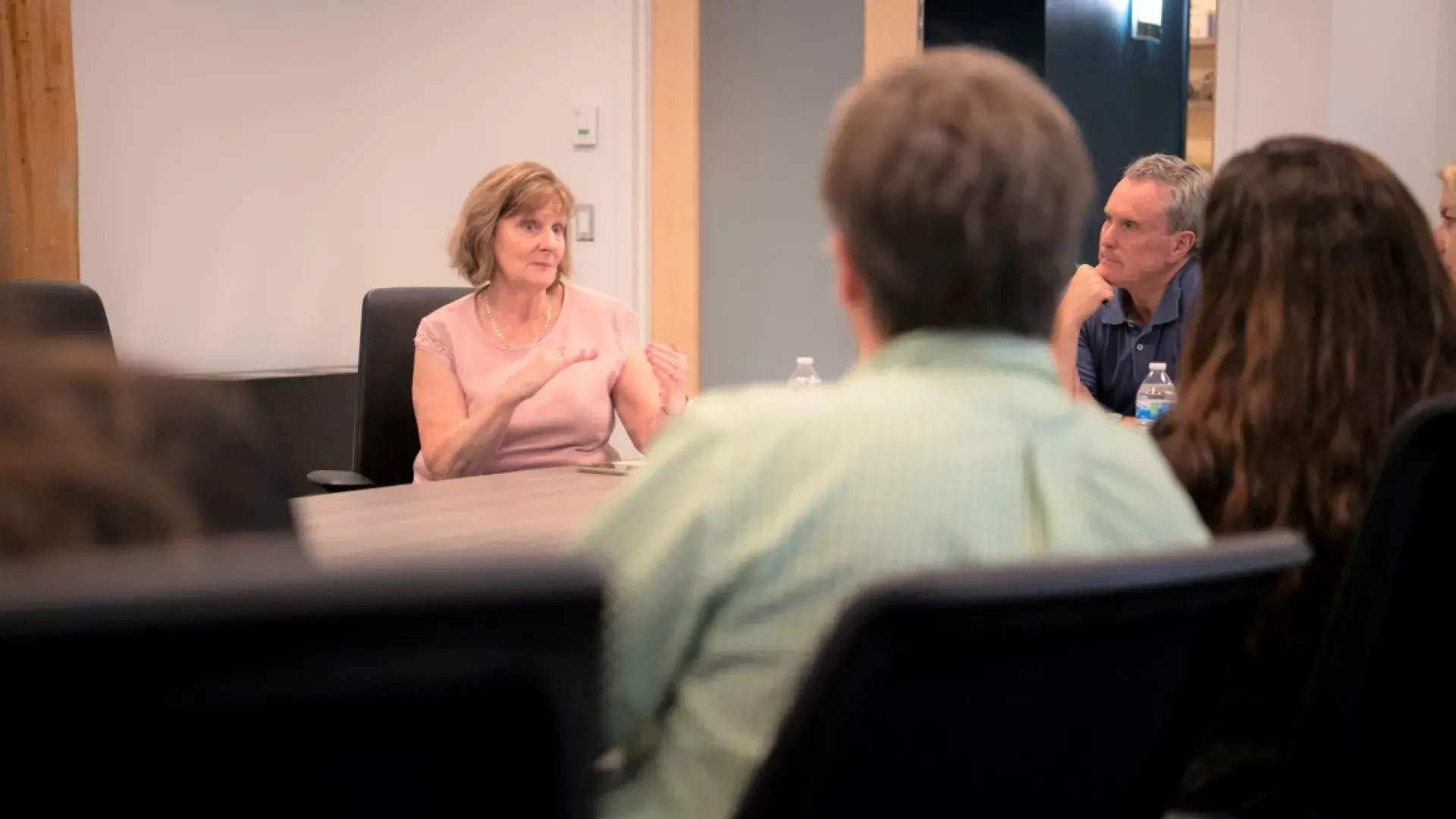 Woman gesturing while speaking to people in a conference room.