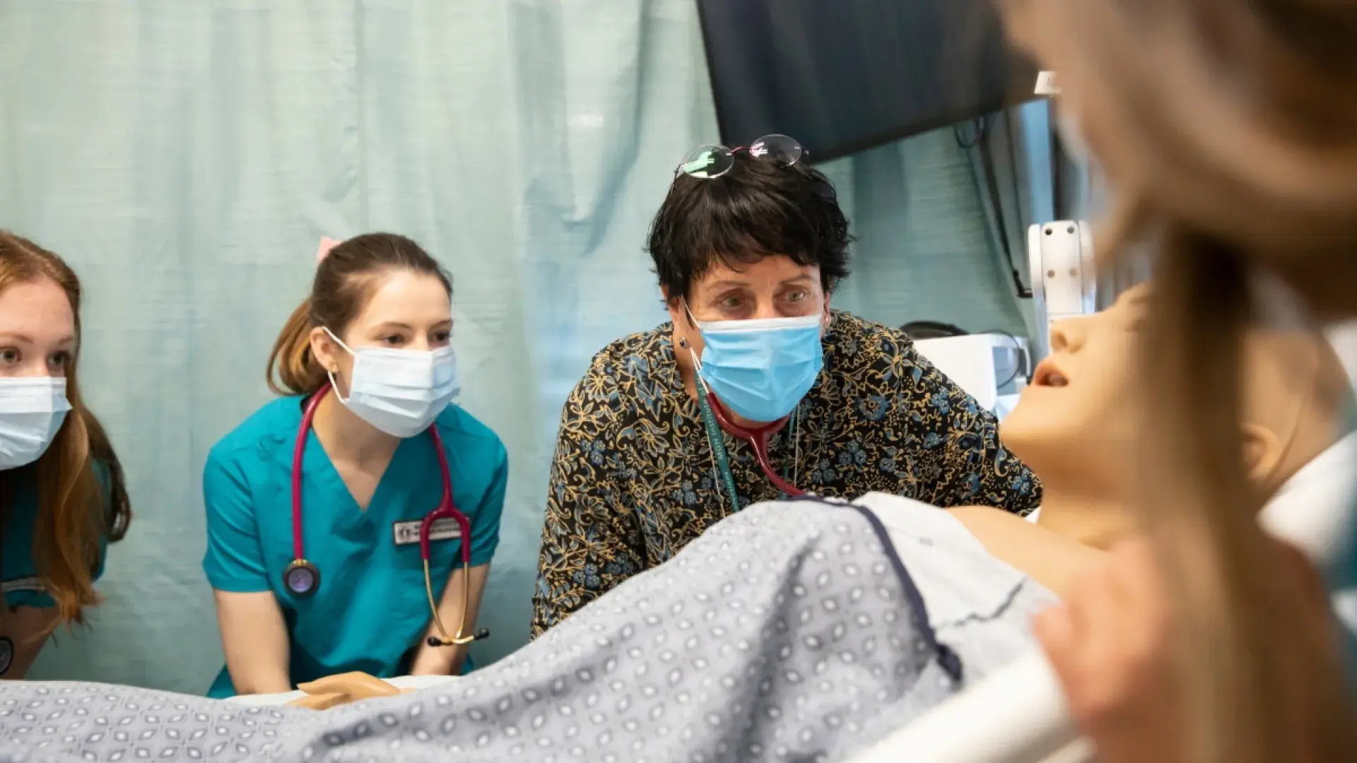 People in masks looking at manikin in a room.