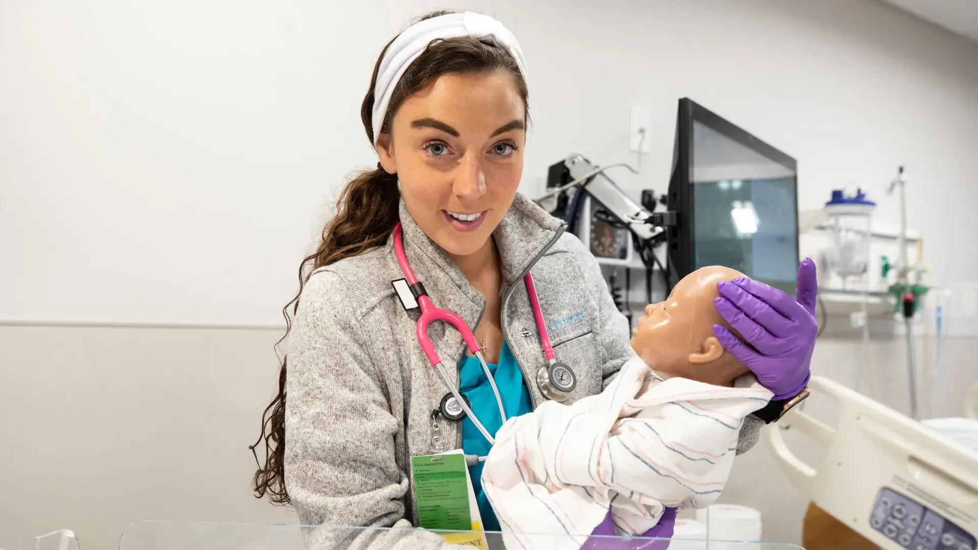 A student in the MGH IHP Fast-Track BSN Program holding an infant mannequin during a hands-on nursing licensure preparation session. The student is dressed in scrubs and is actively participating in the accelerated nursing curriculum, which is part of an intensive nursing training program designed for professionals transitioning to nursing careers.
