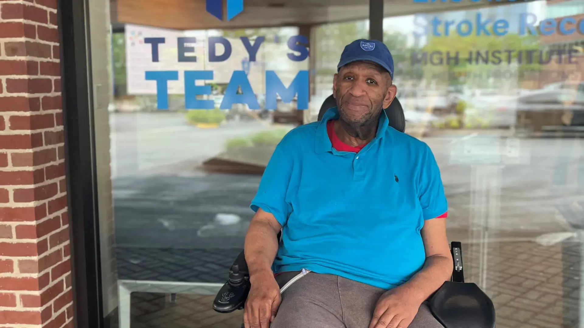 Man sits in wheelchair in front of Tedy's Team sign
