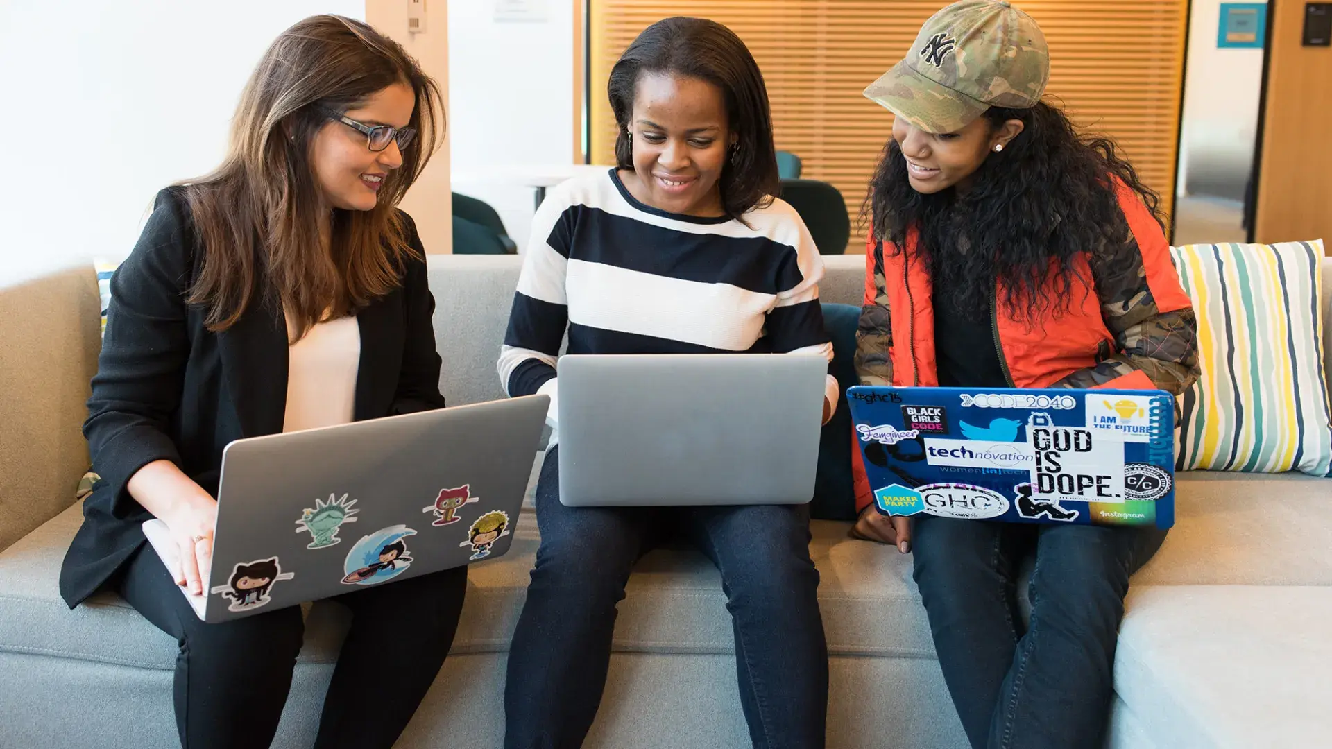 three women sit on a couch with their laptops