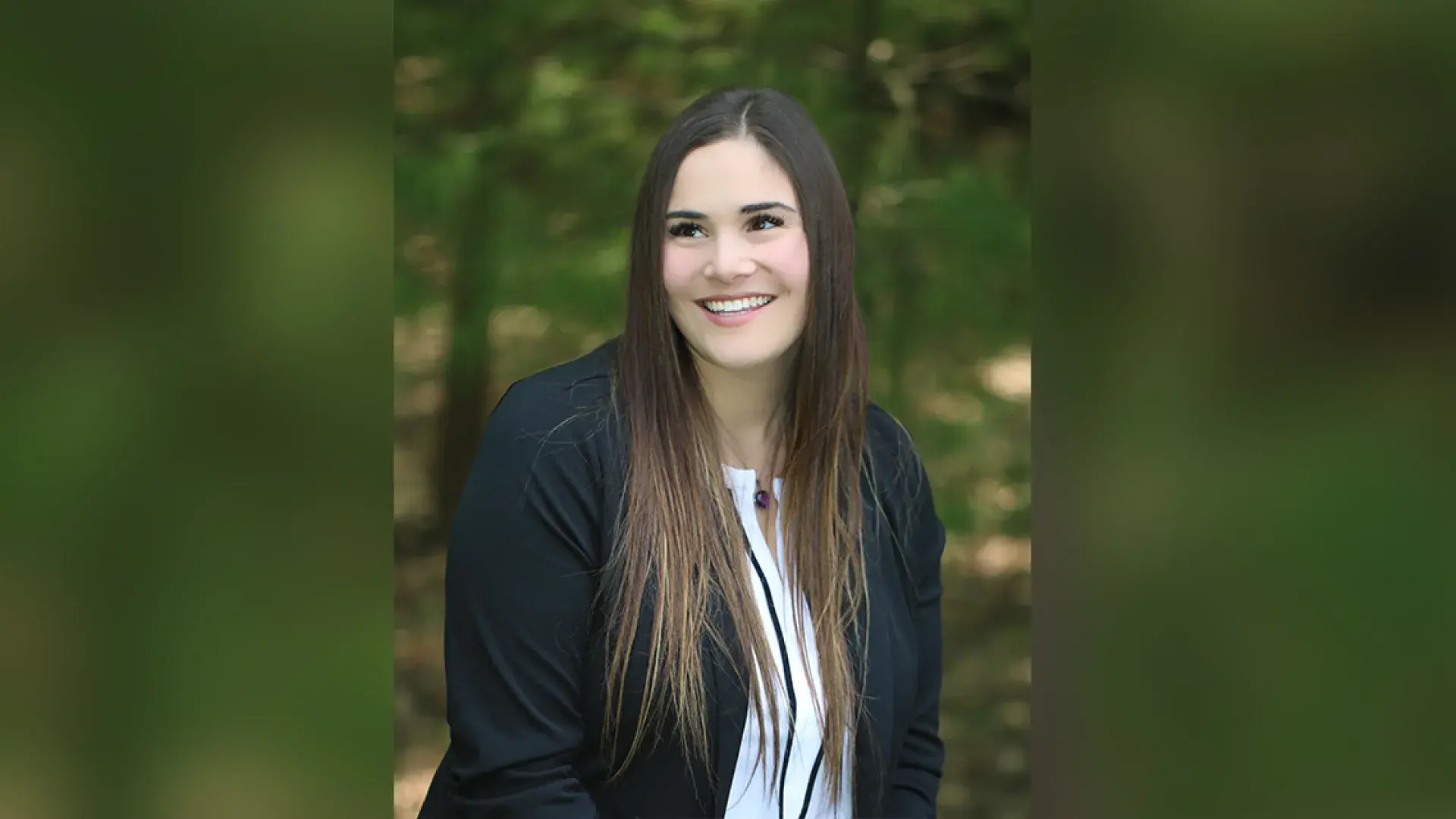 leah is outside in front of trees and she wears a white blouse under a black long sleeve top