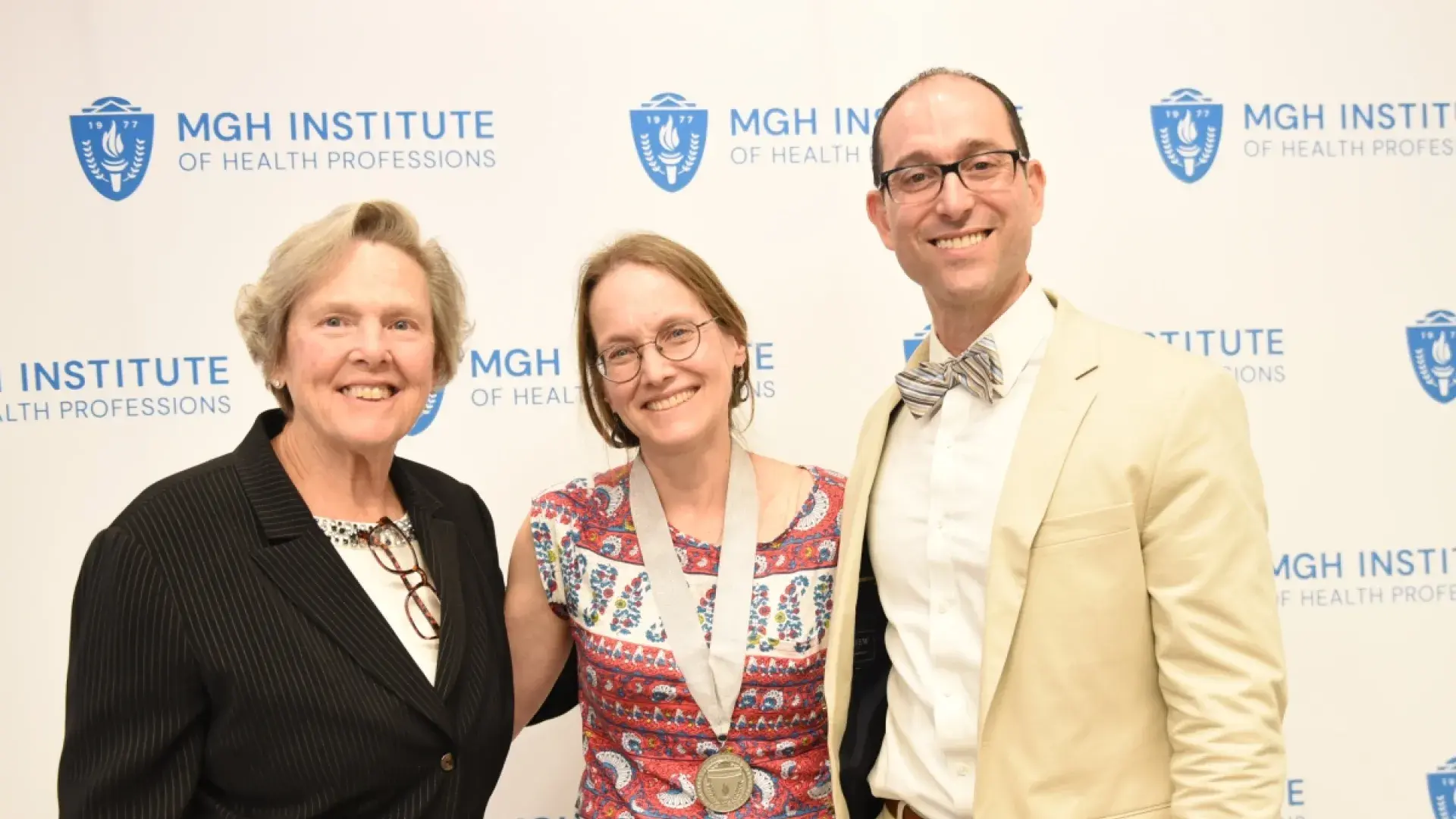 Two women and a man smiling in front of a banner