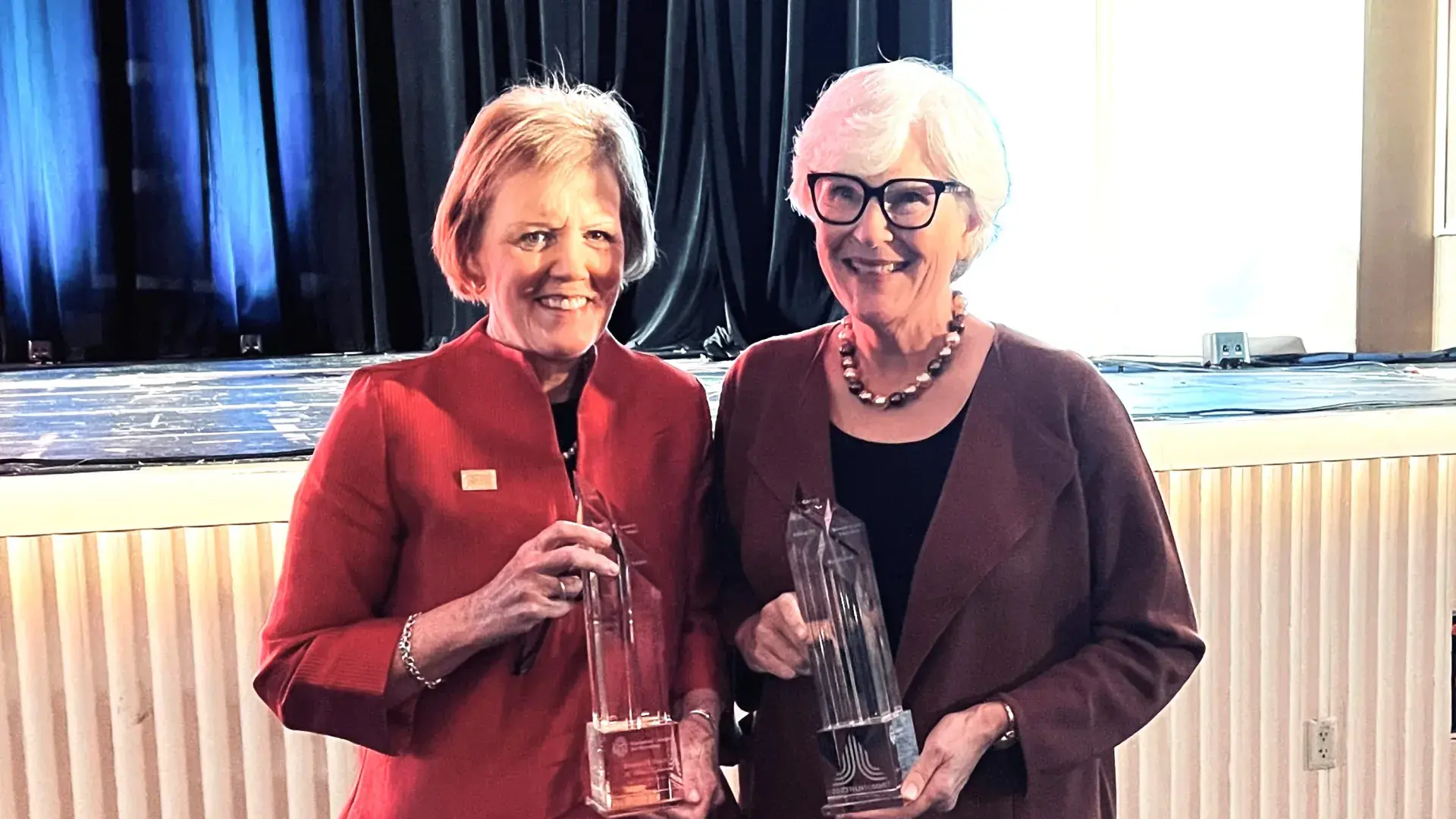 Two women smiling while holding trophies