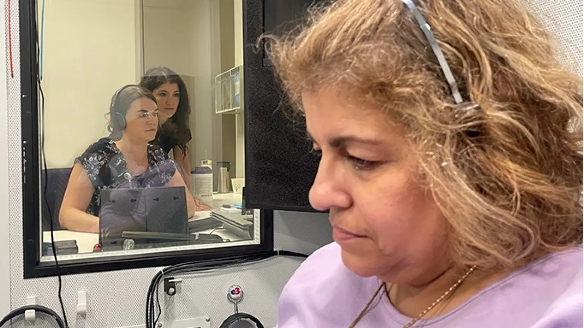 MGH IHP AuD students observing a hearing test conducted in a soundproof booth as part of their hands-on training.