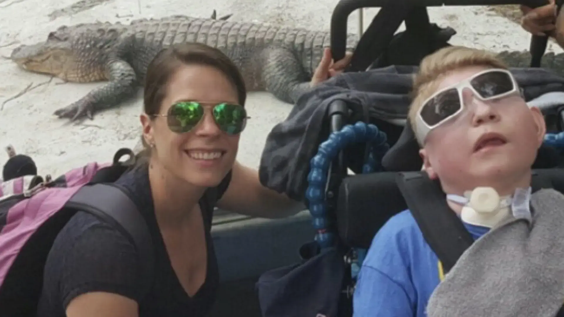 woman stands with man in wheelchair in front of alligator