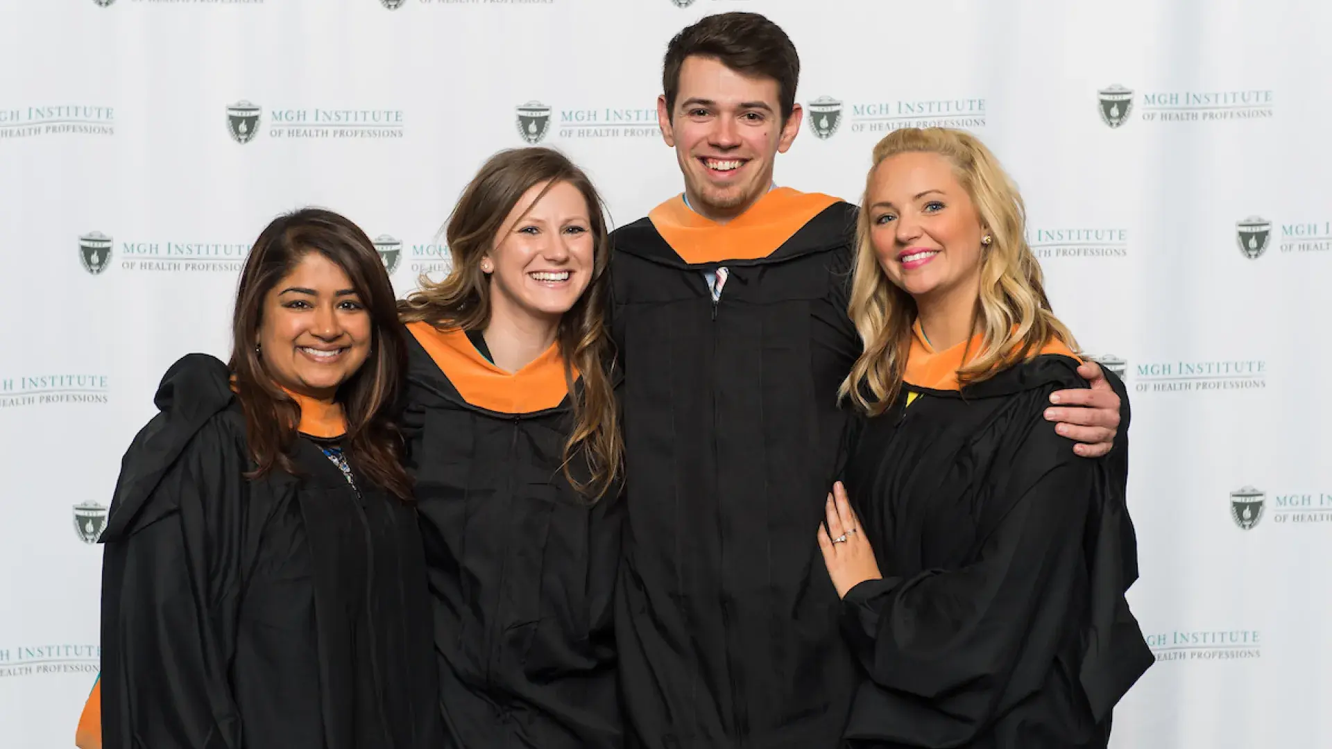 four young-looking people in black graduation gowns with golden collars
