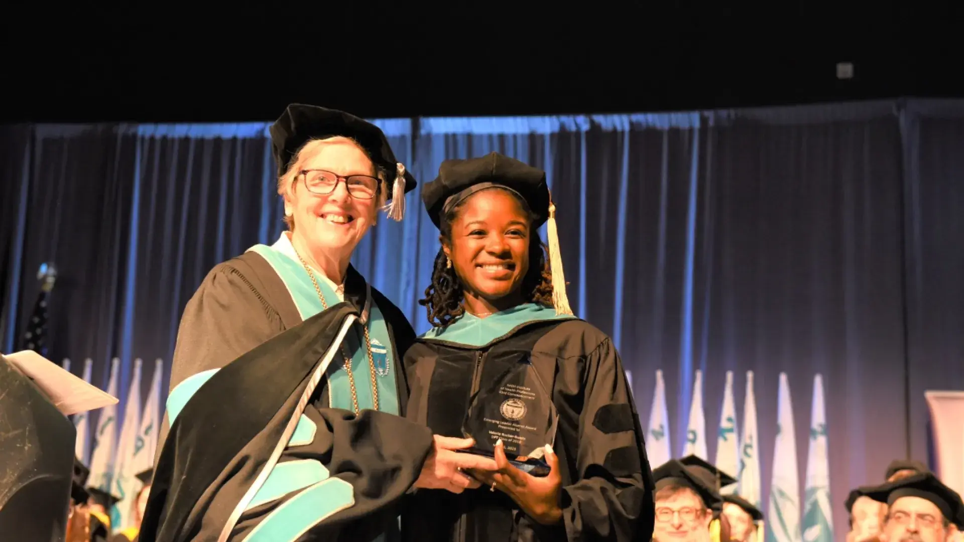 Two women smiling on stage in graduation robes