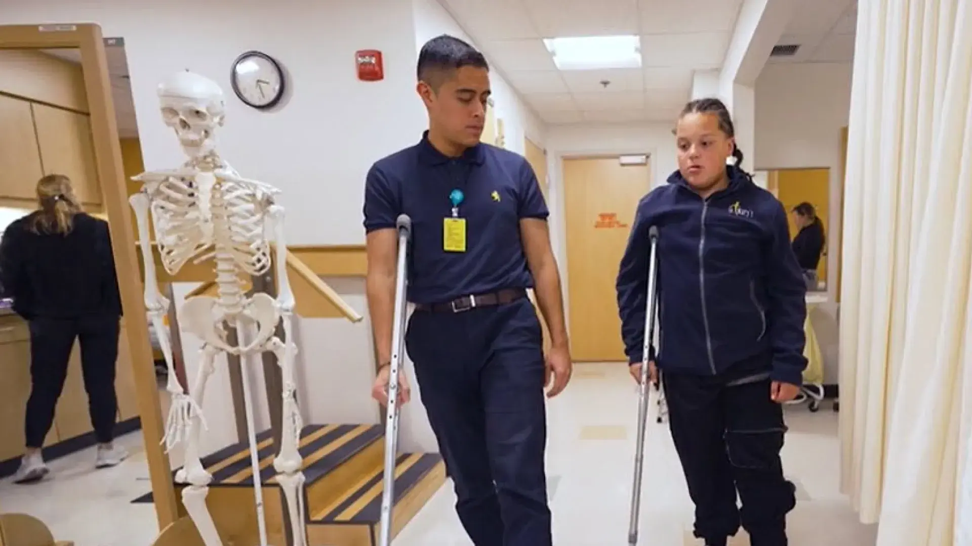 A student and a patient practice walking with crutches in a clinical setting, focusing on physical rehabilitation and patient mobility.