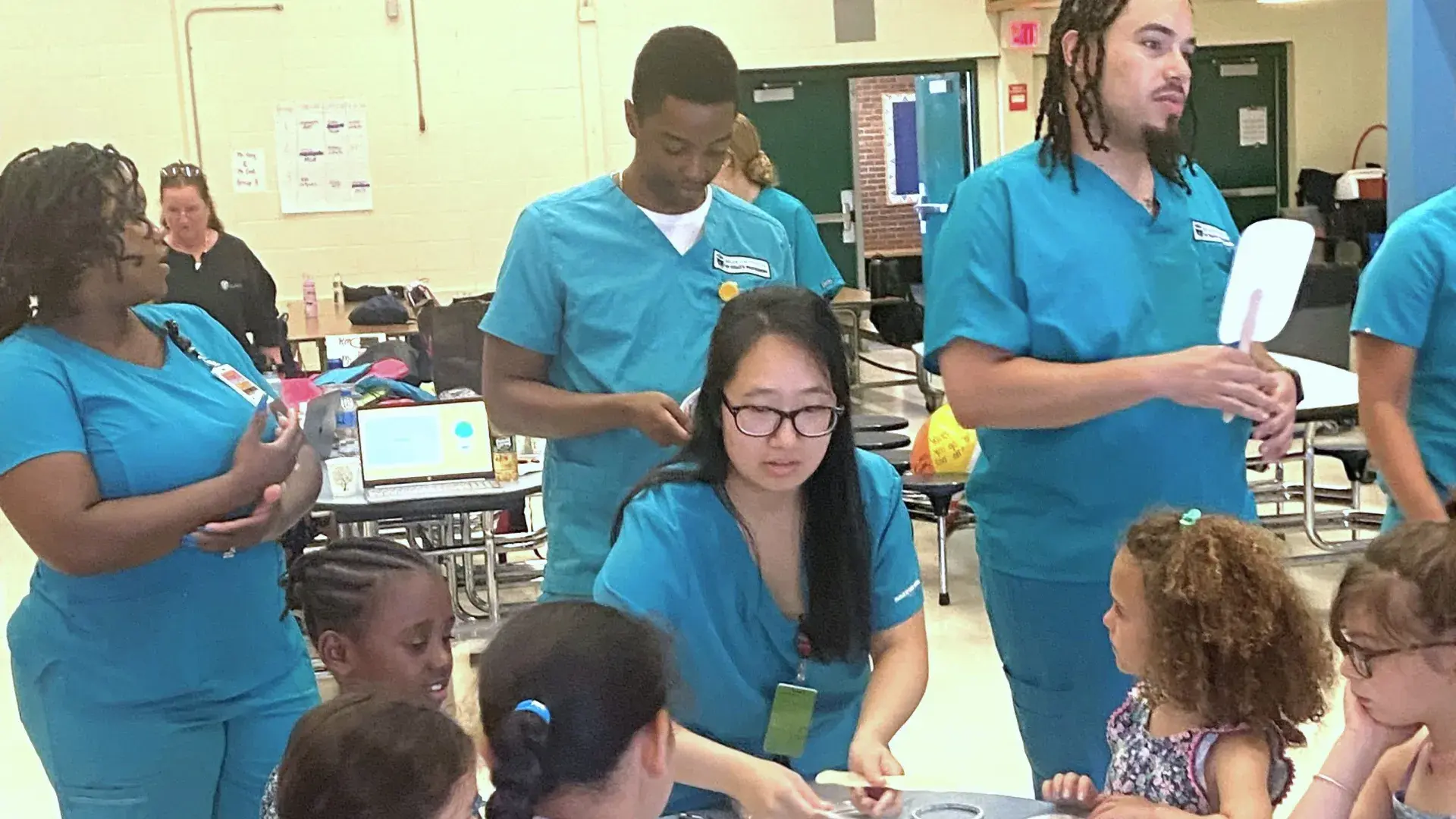 Nursing students in teal working with young kids