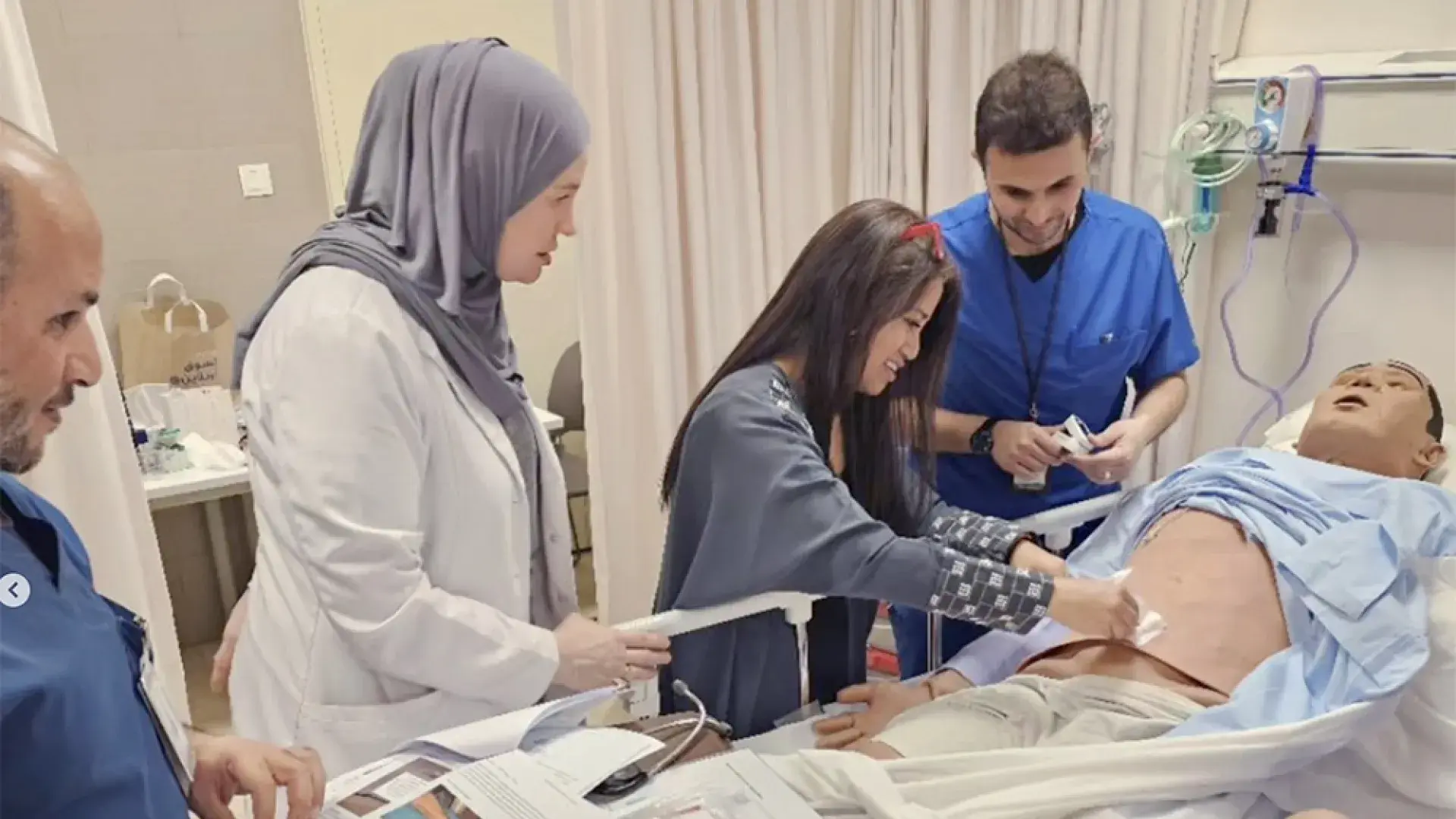 two women and two men place a bandage on a manikin in a bed