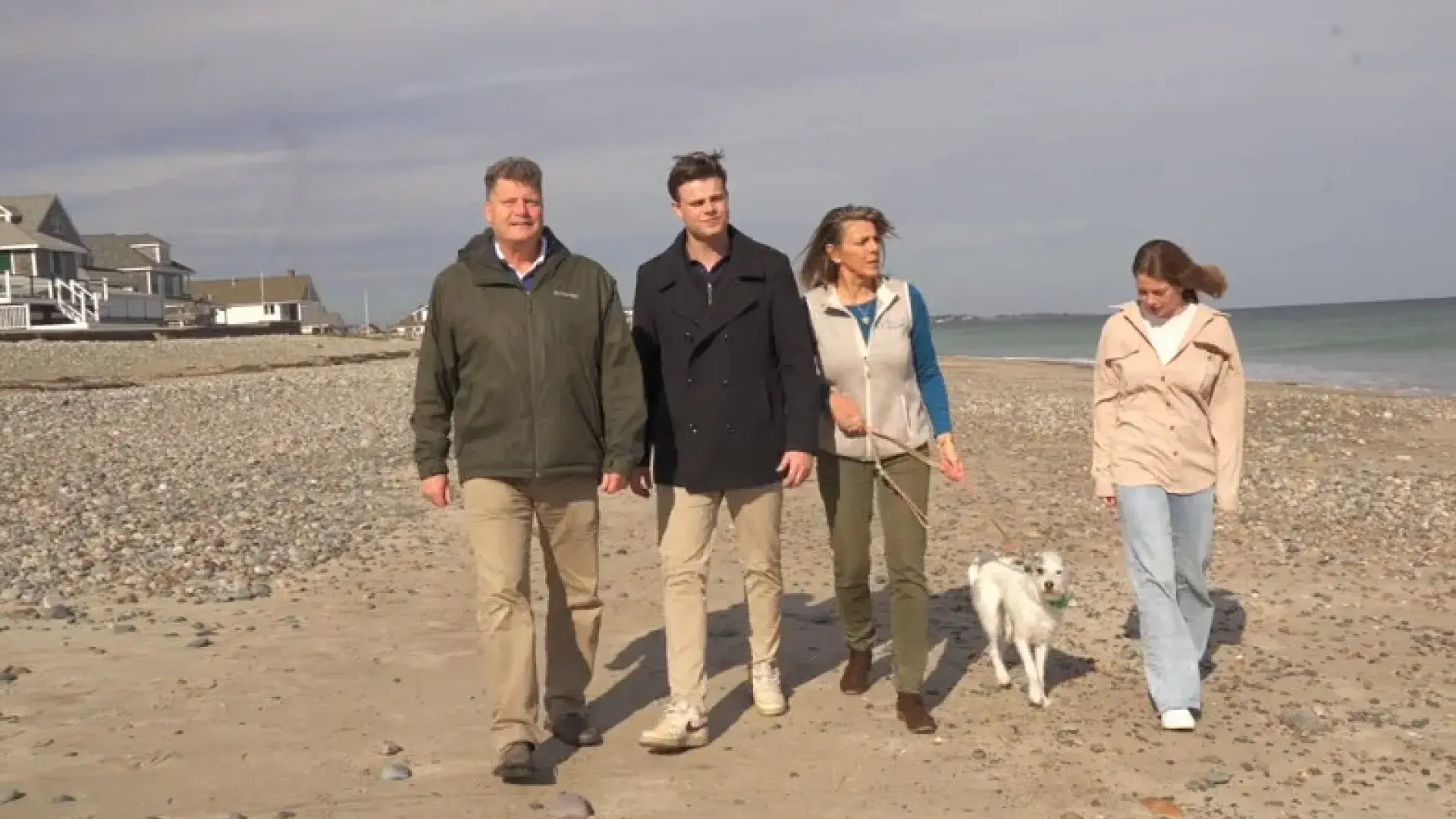 a family of four - mom and dad and teenage son and daughter, walk on a beach with their dog