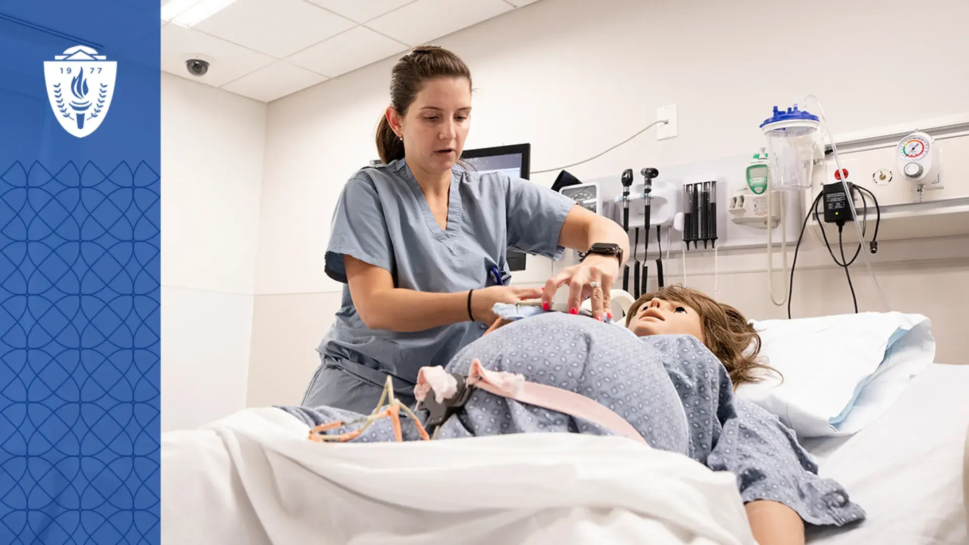 woman in scrubs adjusts a strap on a pregnant manikin in a hospital bed