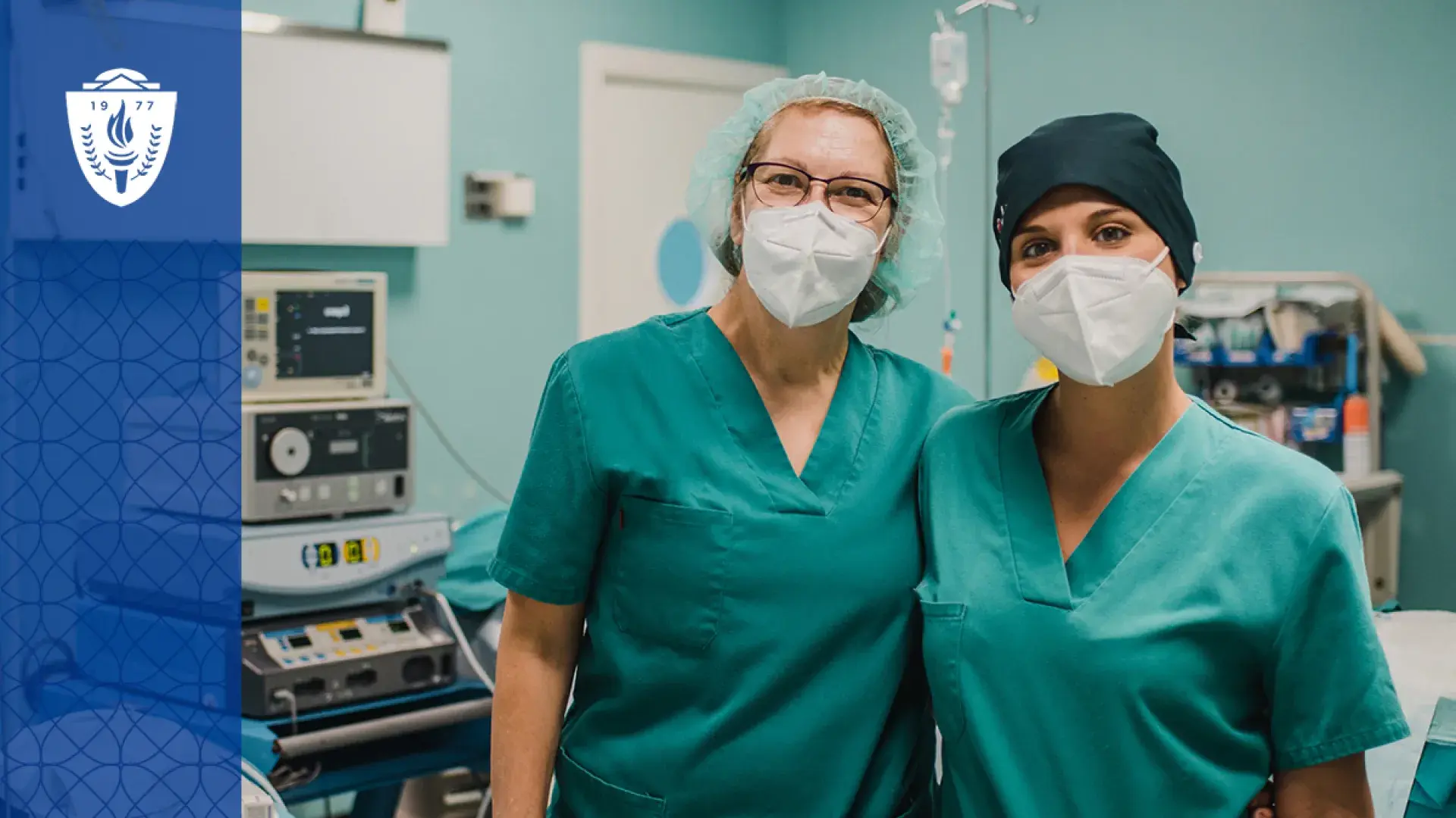two women with masks and green scrubs stand arm and arm