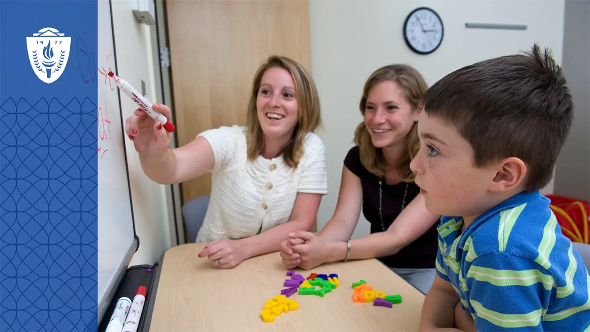 a woman points to a word on a white board while a little boy looks on