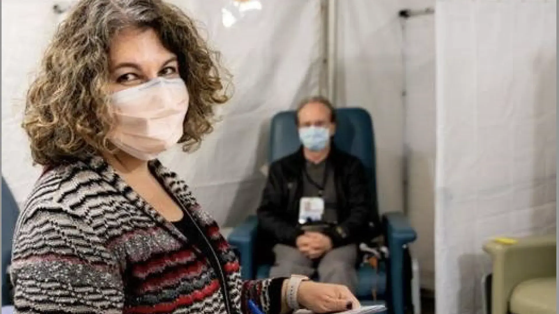 Woman in mask with patient in mask behind her