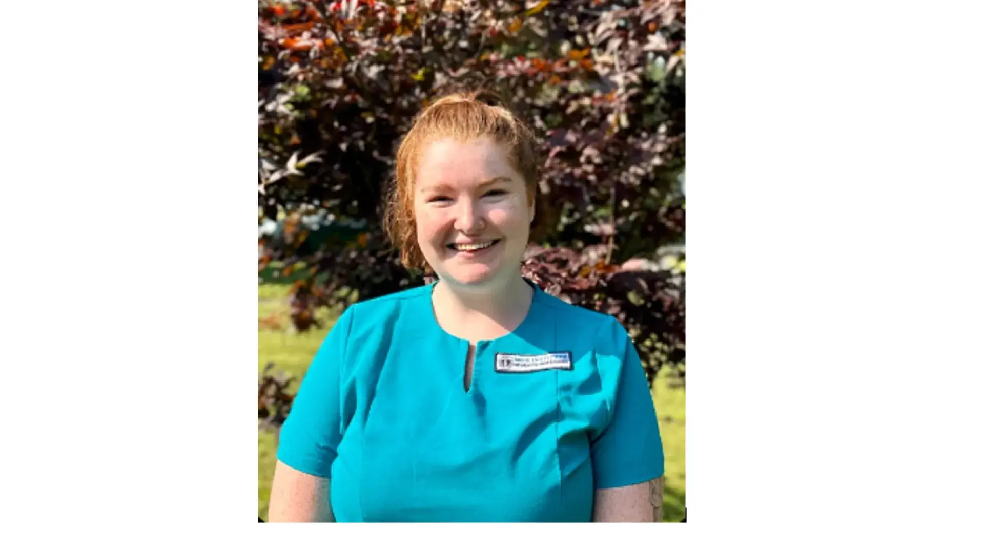 woman stands and smiles while wearing scrubs