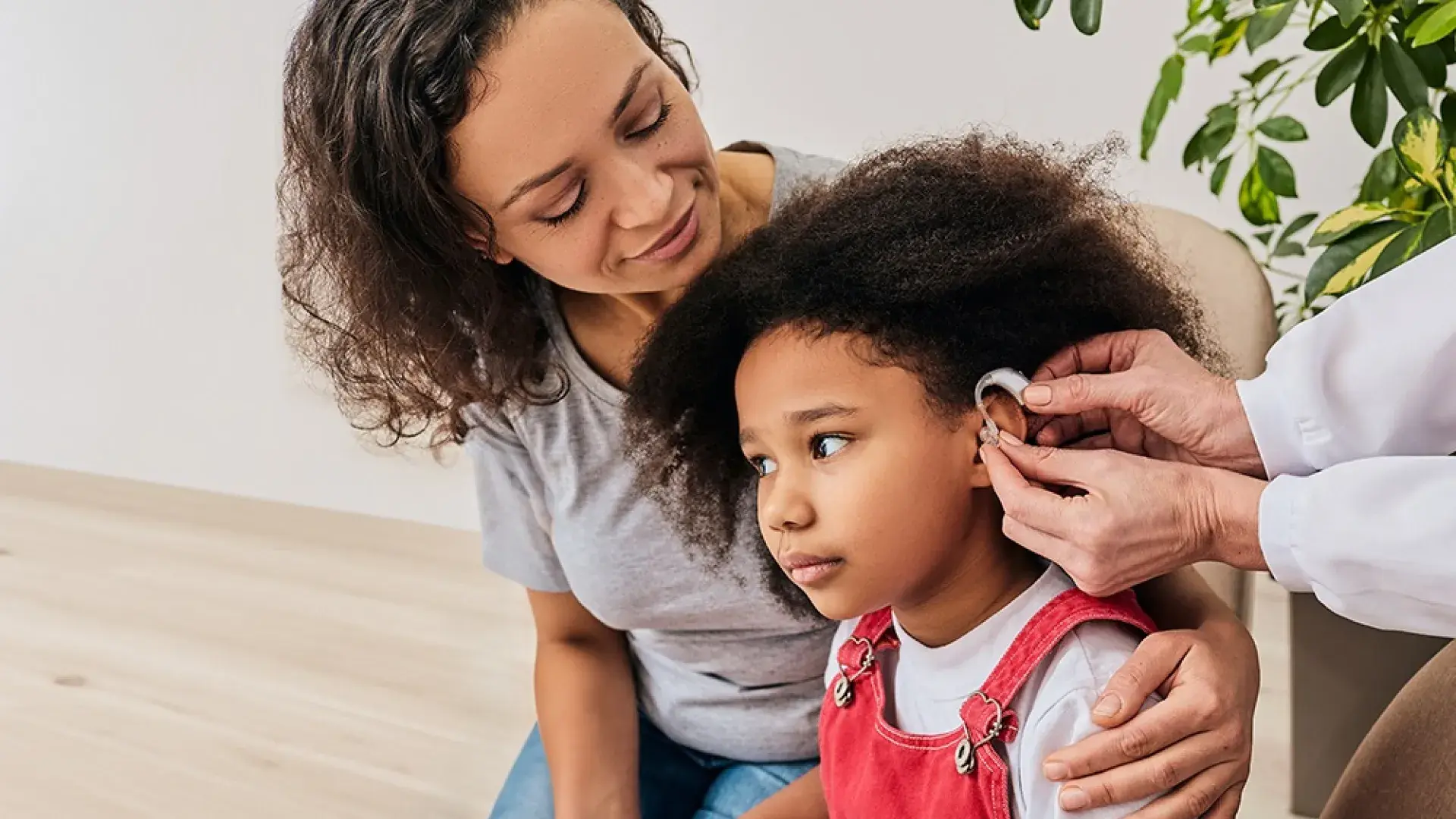 small girl is fitted for a hearing aid while her mom has her arm around her