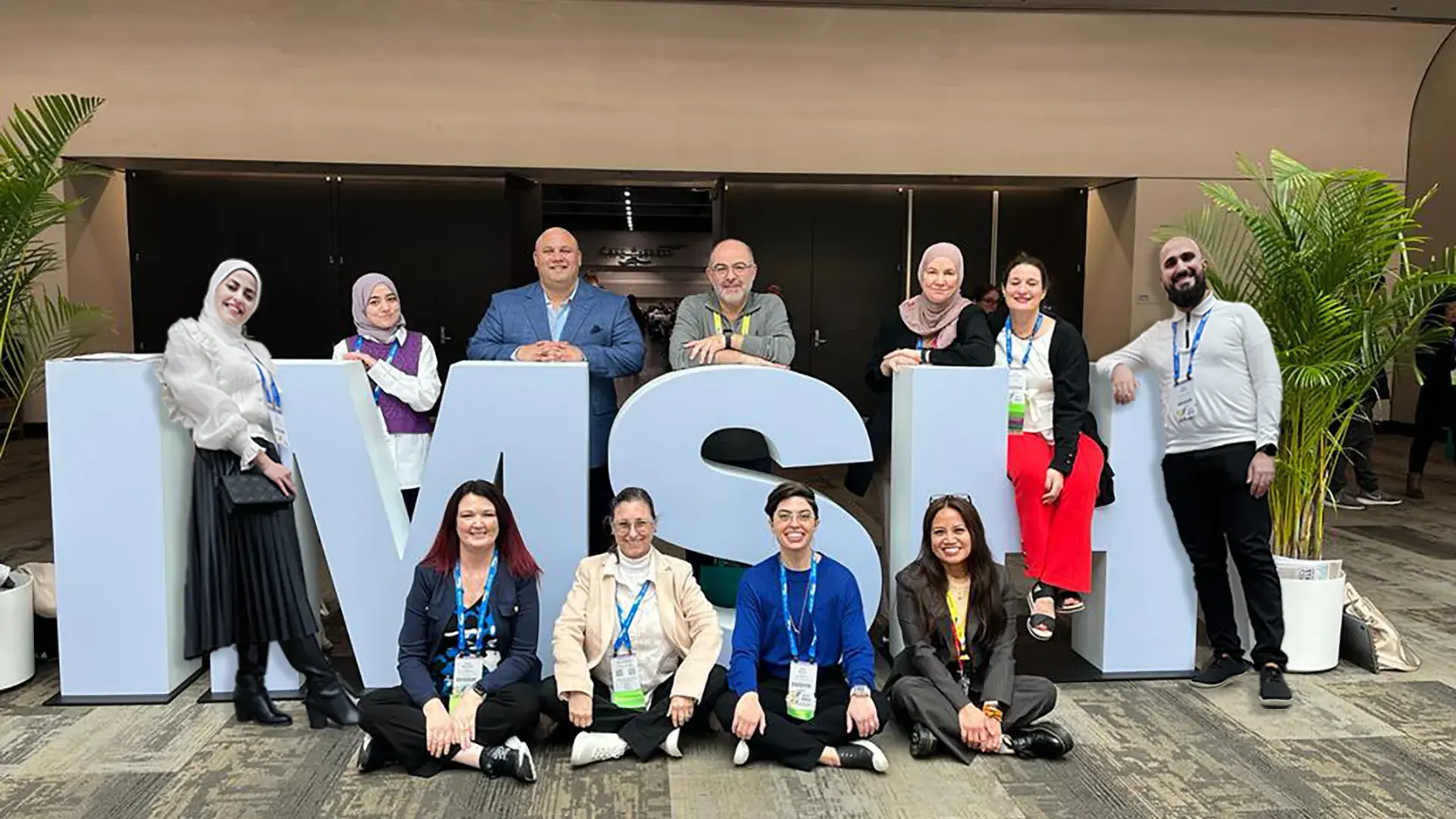 group of people stand in front of and within large letters spelling IMSH