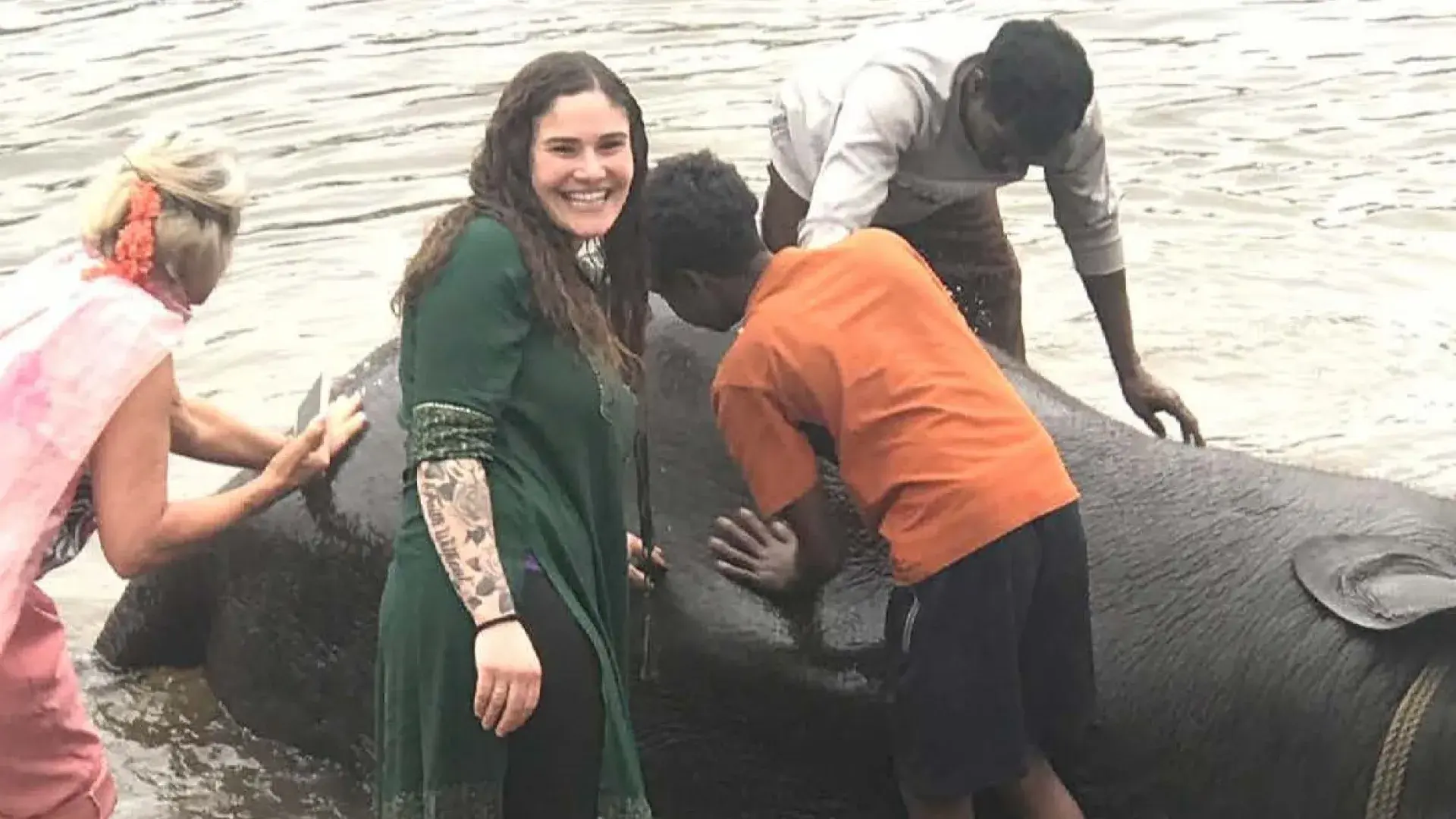 woman smiles as she washes an elephant in a river