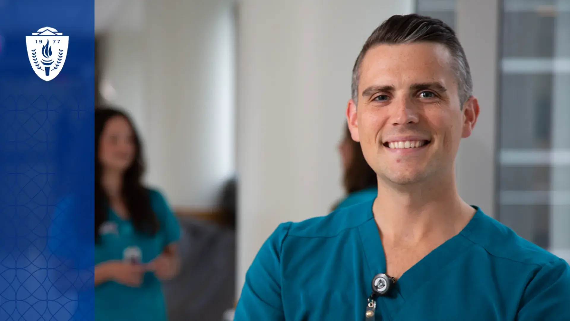 a man smiles in nursing scrubs in the hallway of a hospital